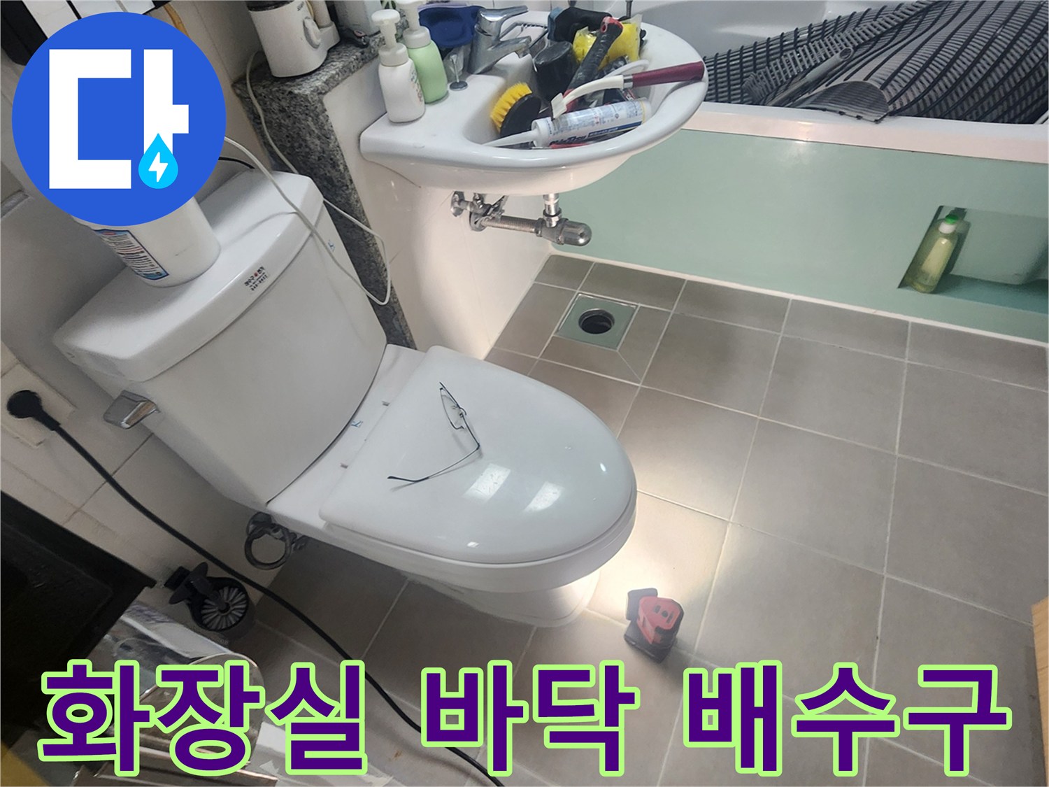 양변기 옆쪽 타일 바닥에 위치한 배수구와 세면대 하부 배관 사진입니다.
