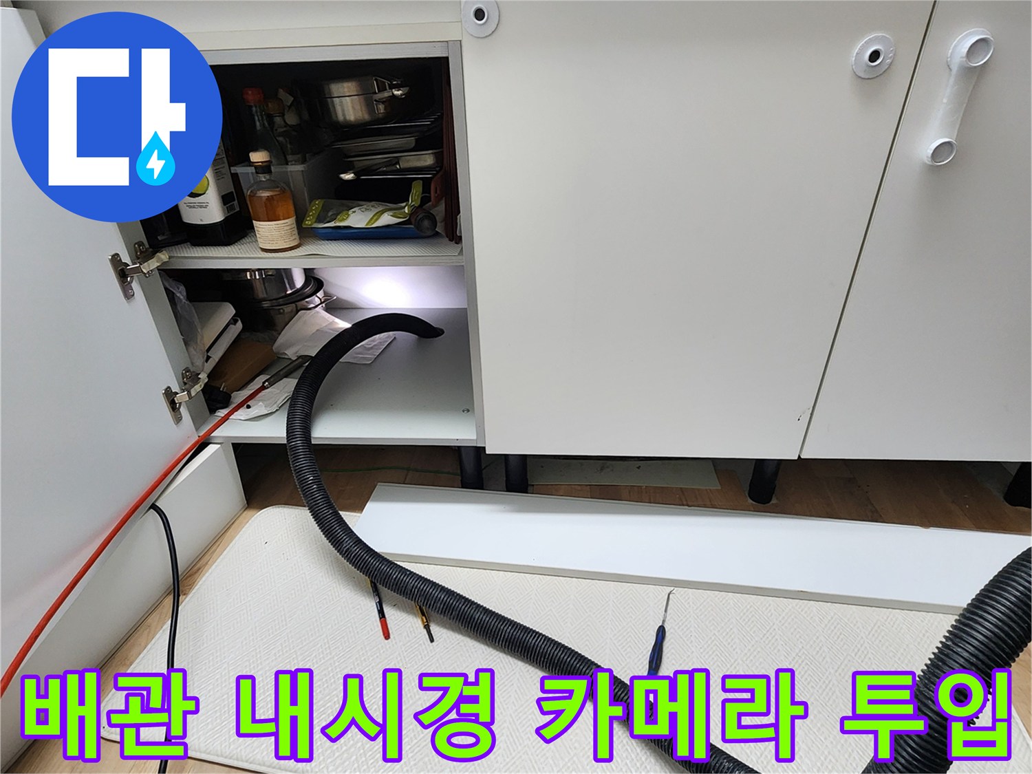 싱크대 하단 배관 내부를 관찰하기 위해 검은색 유연한 내시경 호스를 연결한 사진입니다.
