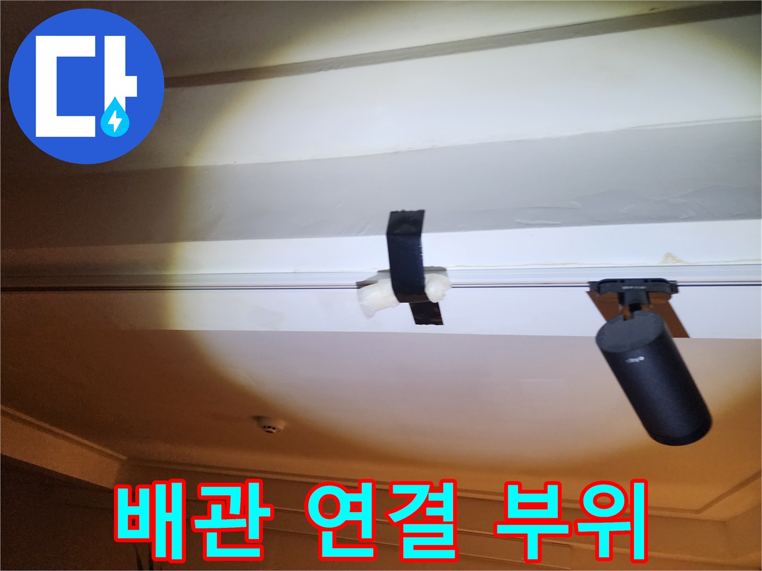 천장 아래로 내려온 배관과 고정용 벨트의 근접 촬영입니다.