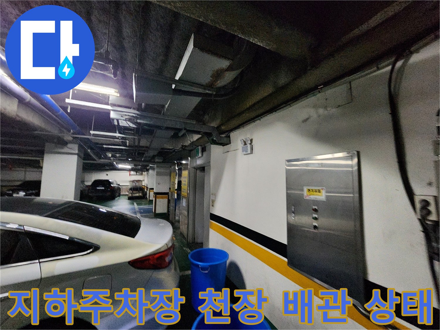 지하 주차장 천장의 노출된 배관과 벽면 전기 분전함 모습입니다.
