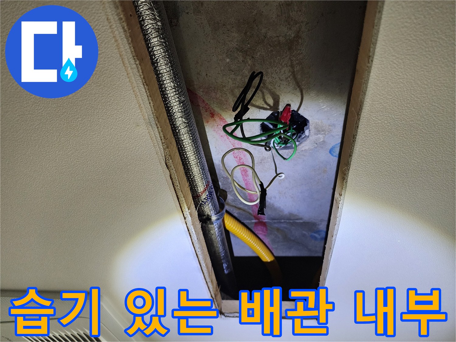 천장 점검구 내부에 노출된 은색 관과 노란 호스 및 전기선