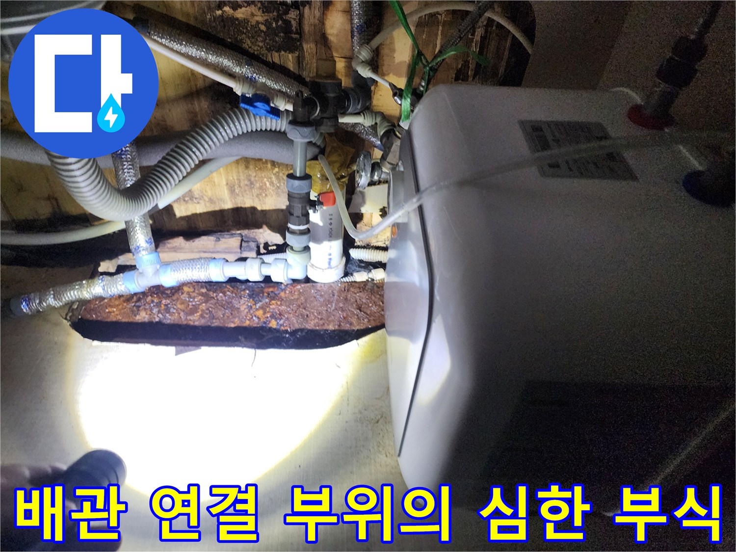 손전등으로 비춘 온수기 주변 배관의 부식 및 습기 상태
