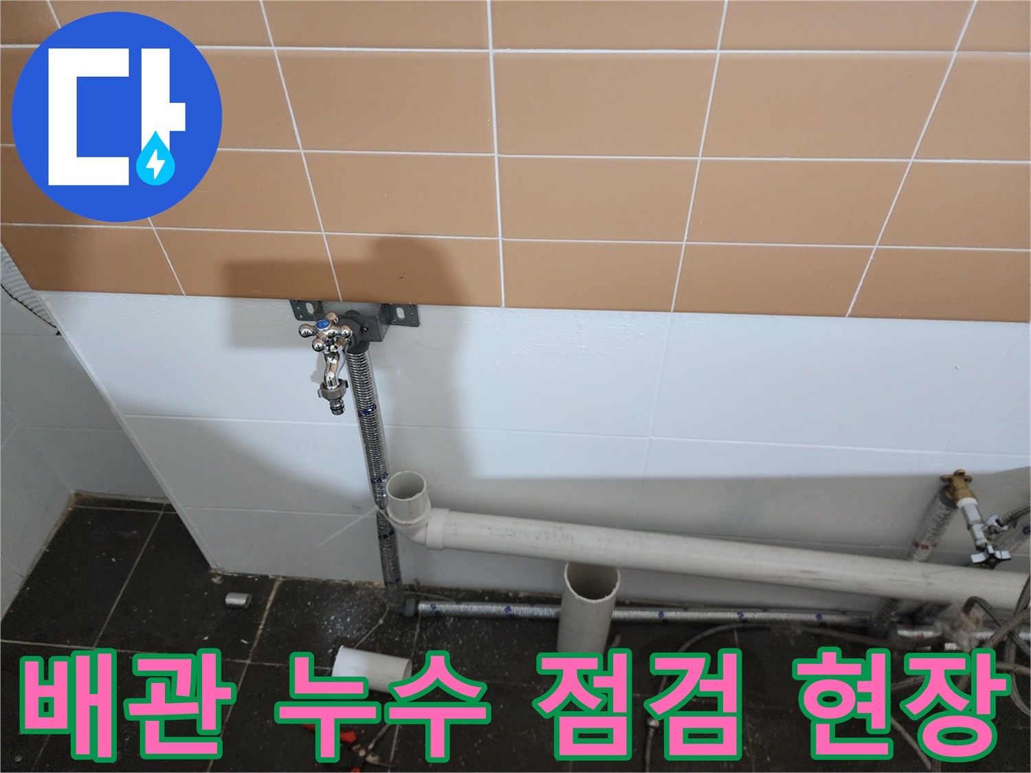 벽면 타일 하단에 노출된 배관과 밸브 장치를 촬영한 이미지입니다.
