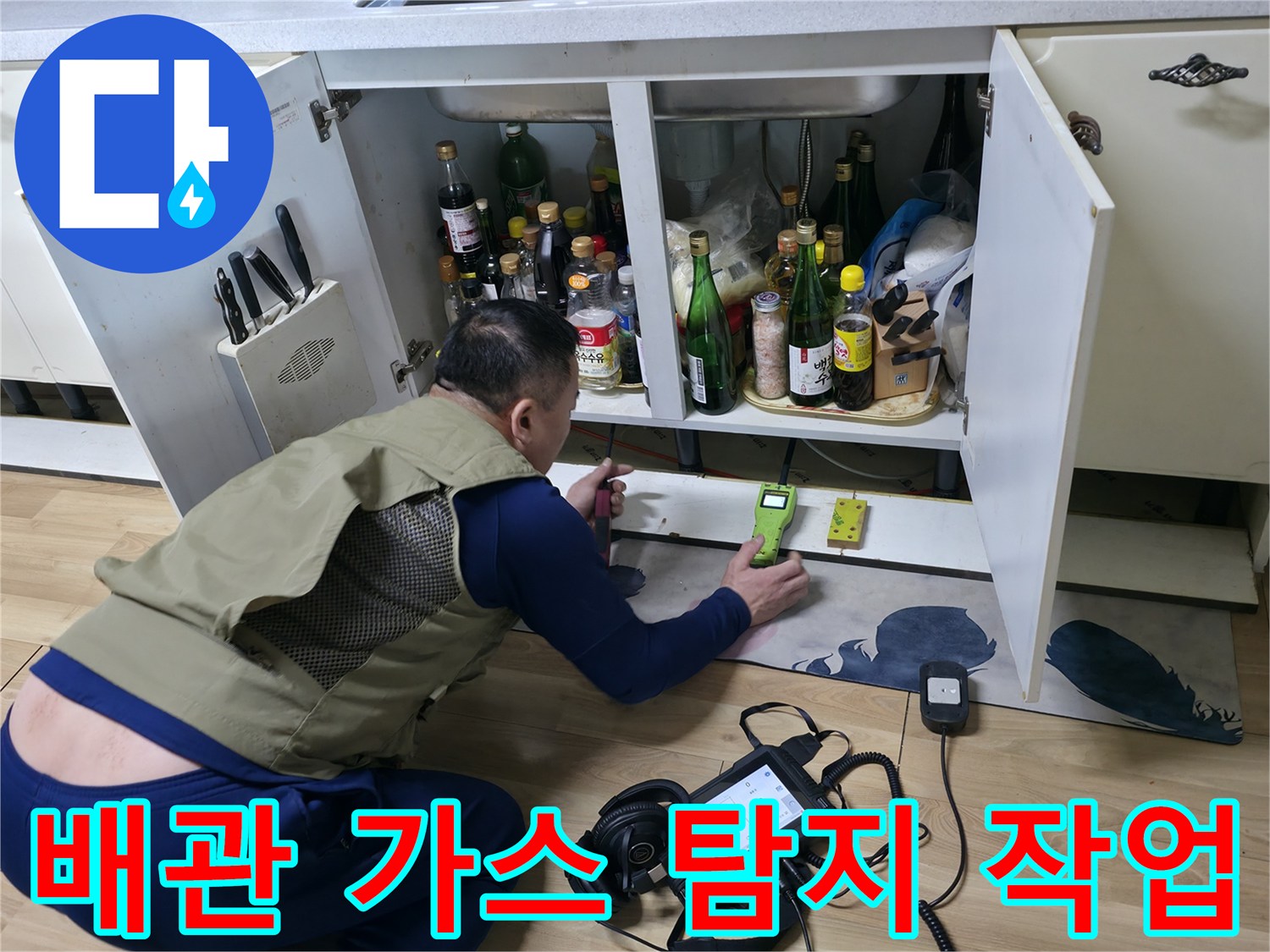 싱크대 밑 배관 누수 지점을 찾기 위해 가스 탐지기를 조작하는 엔지니어의 모습입니다.