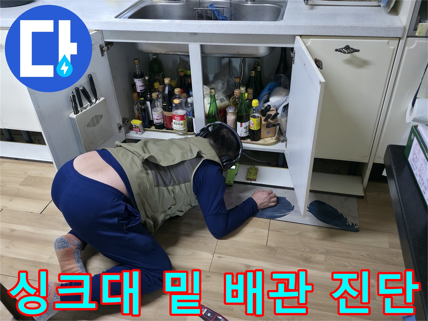 좁은 싱크대 하부 공간에서 배관 누수를 추적하는 엔지니어의 작업 모습