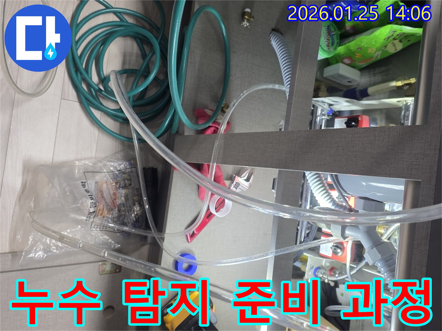배관 누수를 정확히 탐지하기 위한 정밀 준비 과정입니다-싱크대 하부에 다양한 측정 장비와 호스를 설치하여-누수 지점을 찾아낼 준비를 마칩니다.