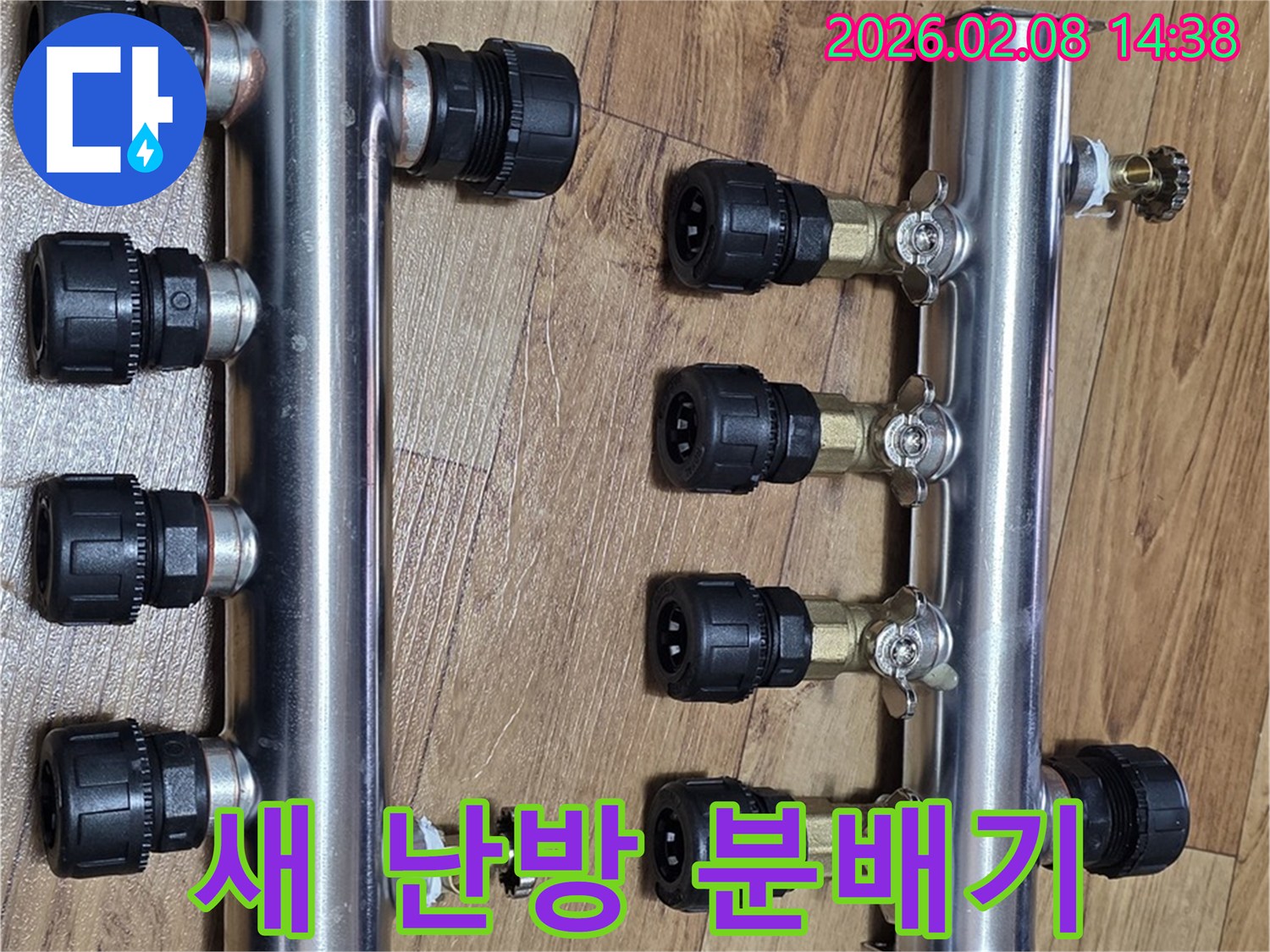 두-개의-새로운-스테인리스-온수분배기가-나무-바닥에-나란히-놓여-있으며-각각-여러-개의-검은색-연결-부품과-금색-밸브를-갖추고-있습니다