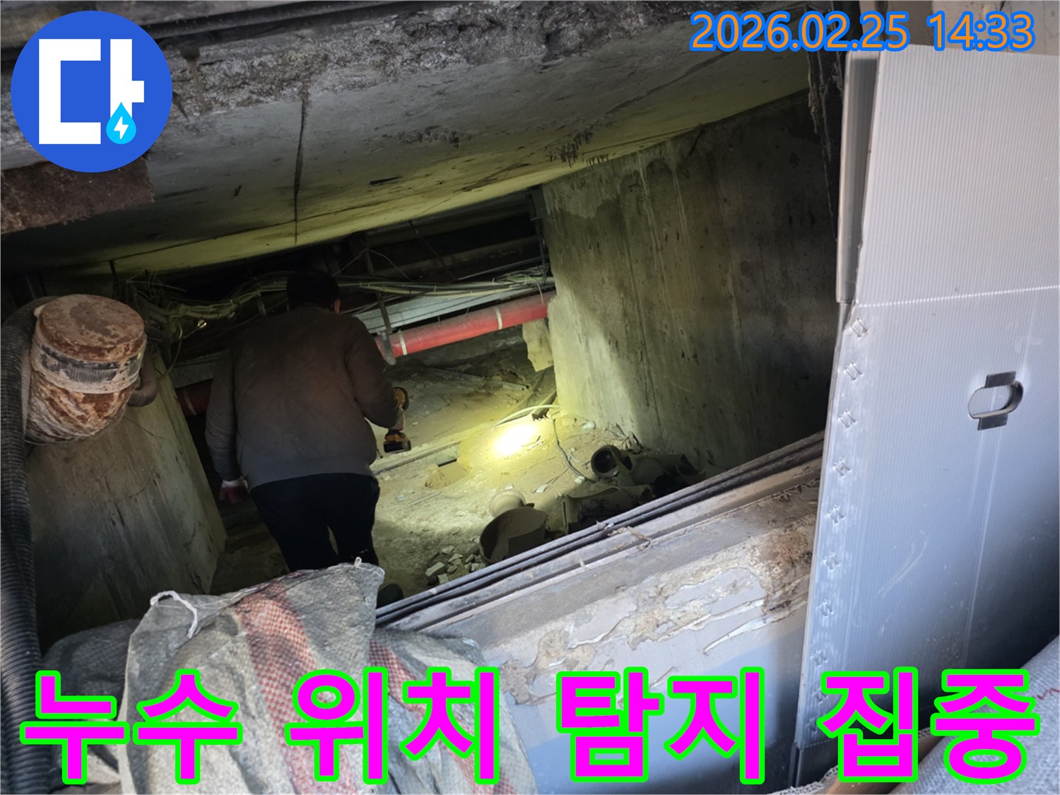 누수 전문 엔지니어가-어둡고 좁은 공간에서-손전등을 비춰가며-누수 발생의 정확한 위치를-탐지하기 위해-집중하는 모습입니다.