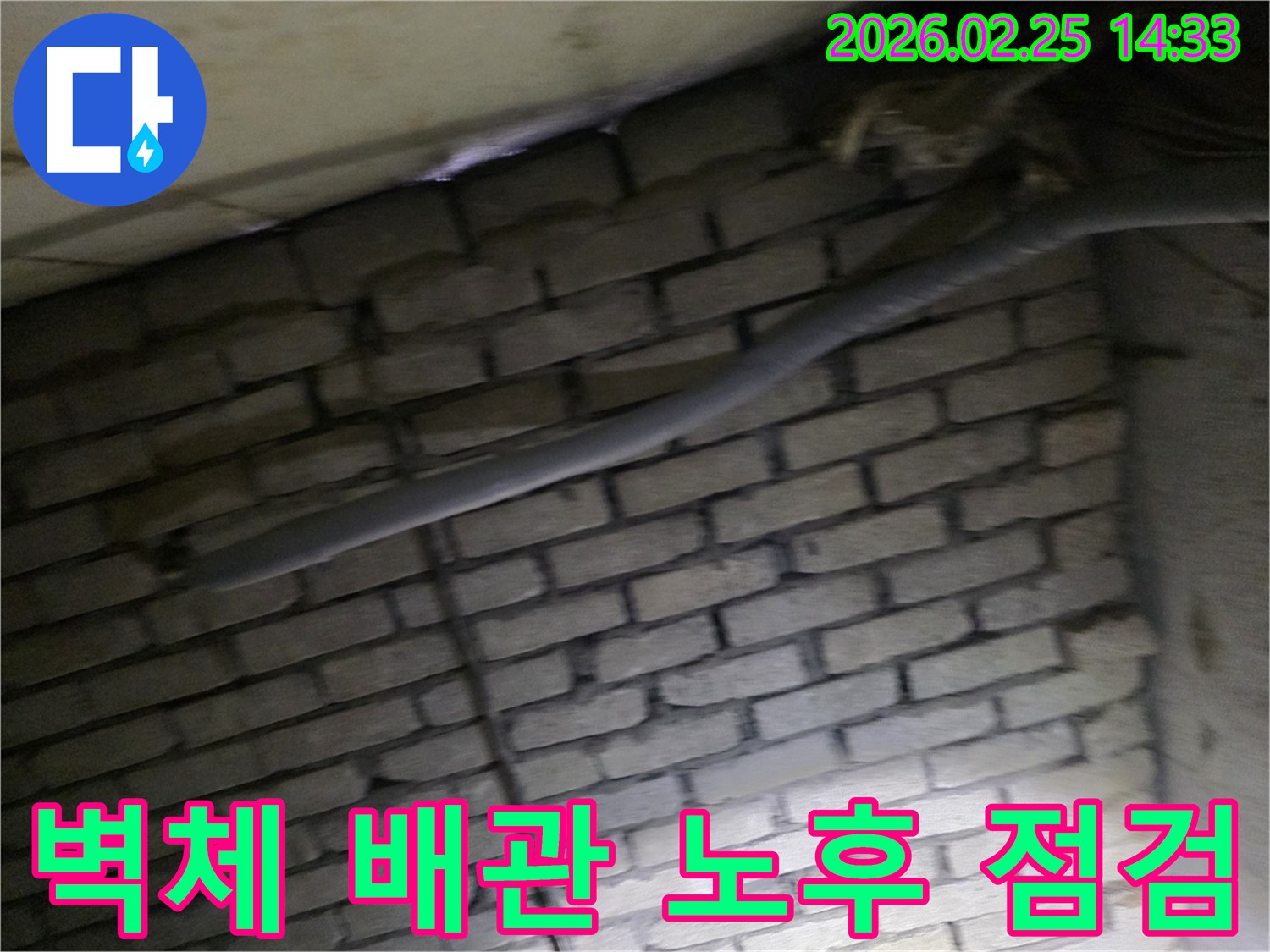 벽돌 벽면을 배경으로-단열된 파이프와 여러 배선이-어두운 공간에서 누수 여부를-확인하기 위해 촬영된 사진입니다.