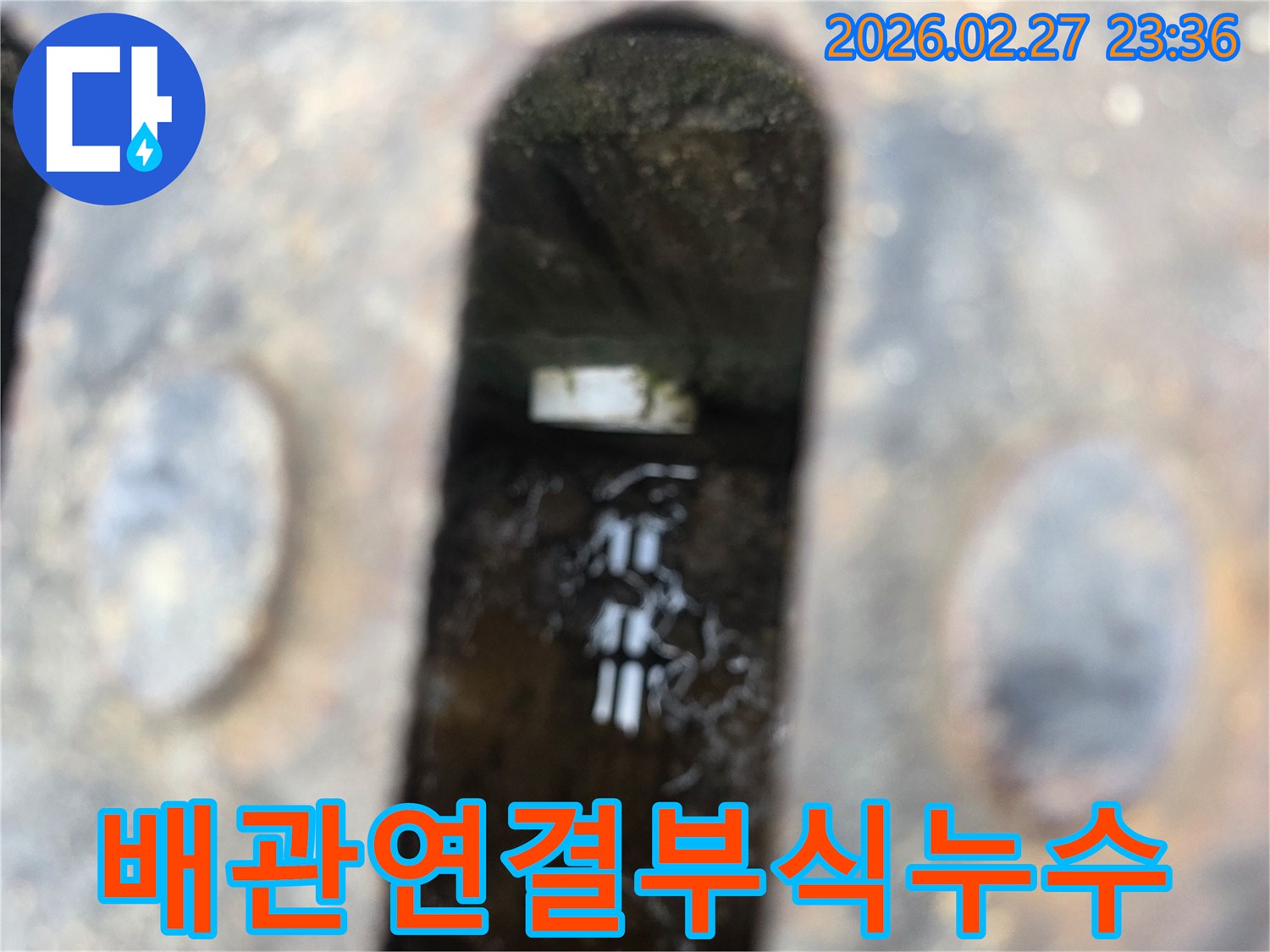 녹슨-철제-덮개-아래-고인-물과-물속에-잠긴-부식된-배관-연결부가-보이는-누수-현장