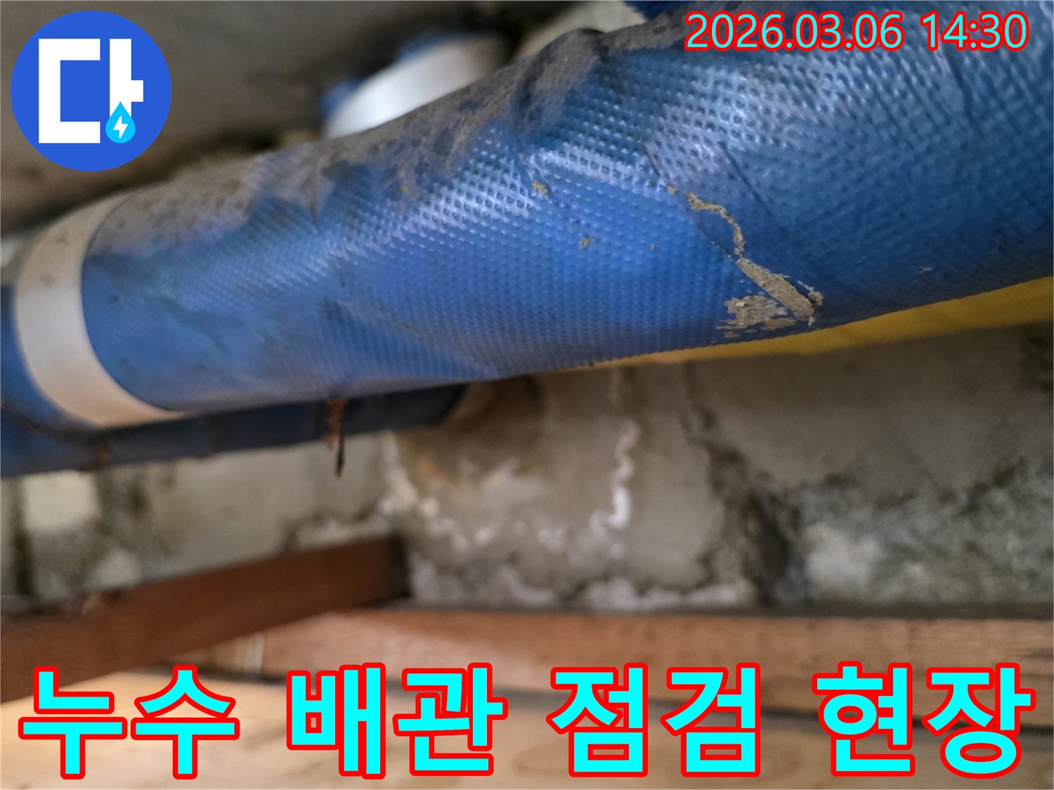 어두운 공간에서-파란색 배관과-젖은 콘크리트 벽면-그리고 나무 구조물을-조사하는 장면