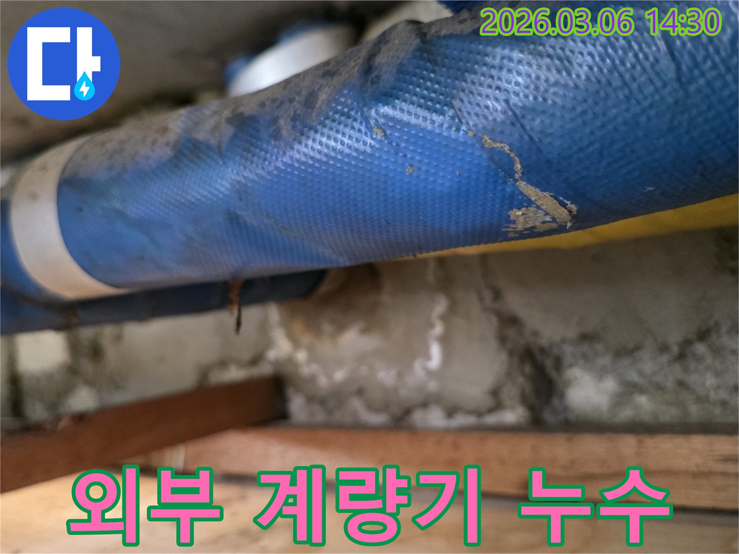 주택 외부-파란색 수도 계량기 배관과-젖은 콘크리트 벽면-그리고 나무 지지대를-꼼꼼히 점검하는 모습