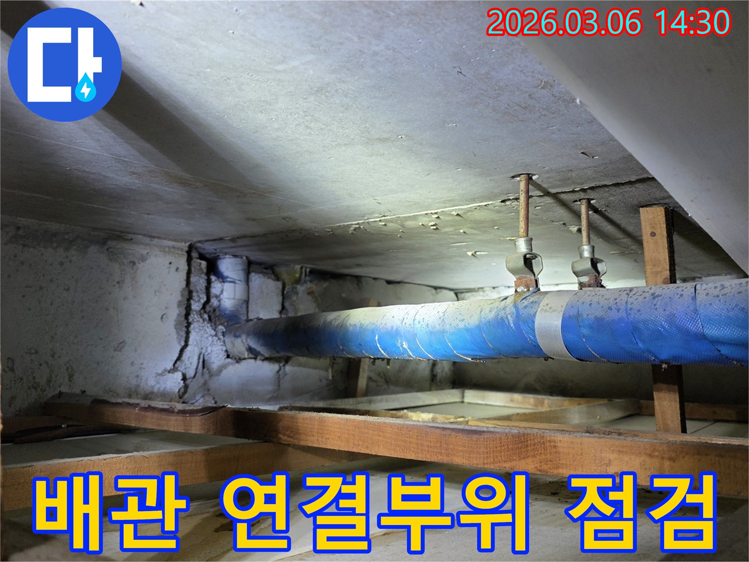 지하 공간의 파란색 배관과-손상된 콘크리트 벽면의-연결 부위를-누수 엔지니어가-정밀하게 점검하는 모습