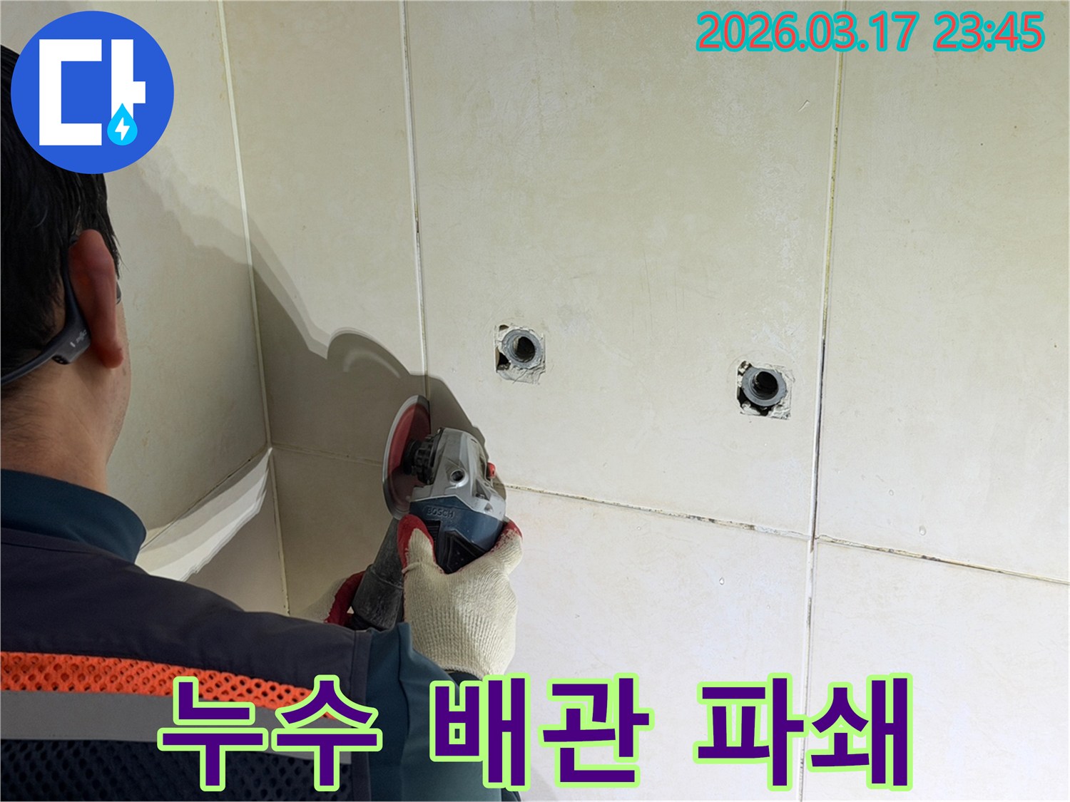 누수된 배관을-노출시키기 위해-전문가가-타일 벽면을-그라인더로-조심스럽게-파쇄하고-있습니다