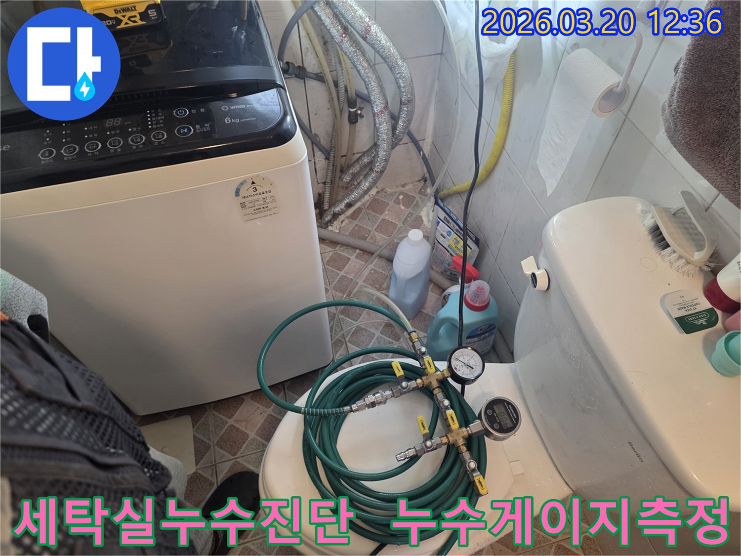 누수 엔지니어가 세탁기와 변기 사이 공간에서-배관 압력 검사 장비를 사용하여-누수 원인을 정밀하게 탐지하고 있습니다