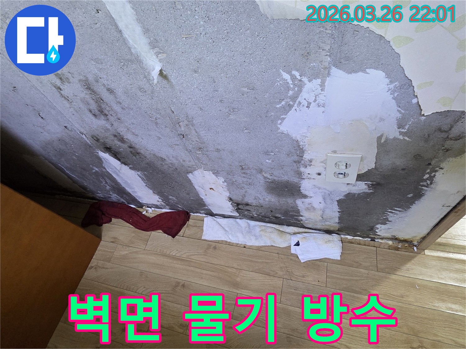 물에-젖어-벽지가-손상되고-곰팡이가-피어있는-콘크리트-벽면-아래-물기를-흡수하는-수건이-놓인-누수-현장