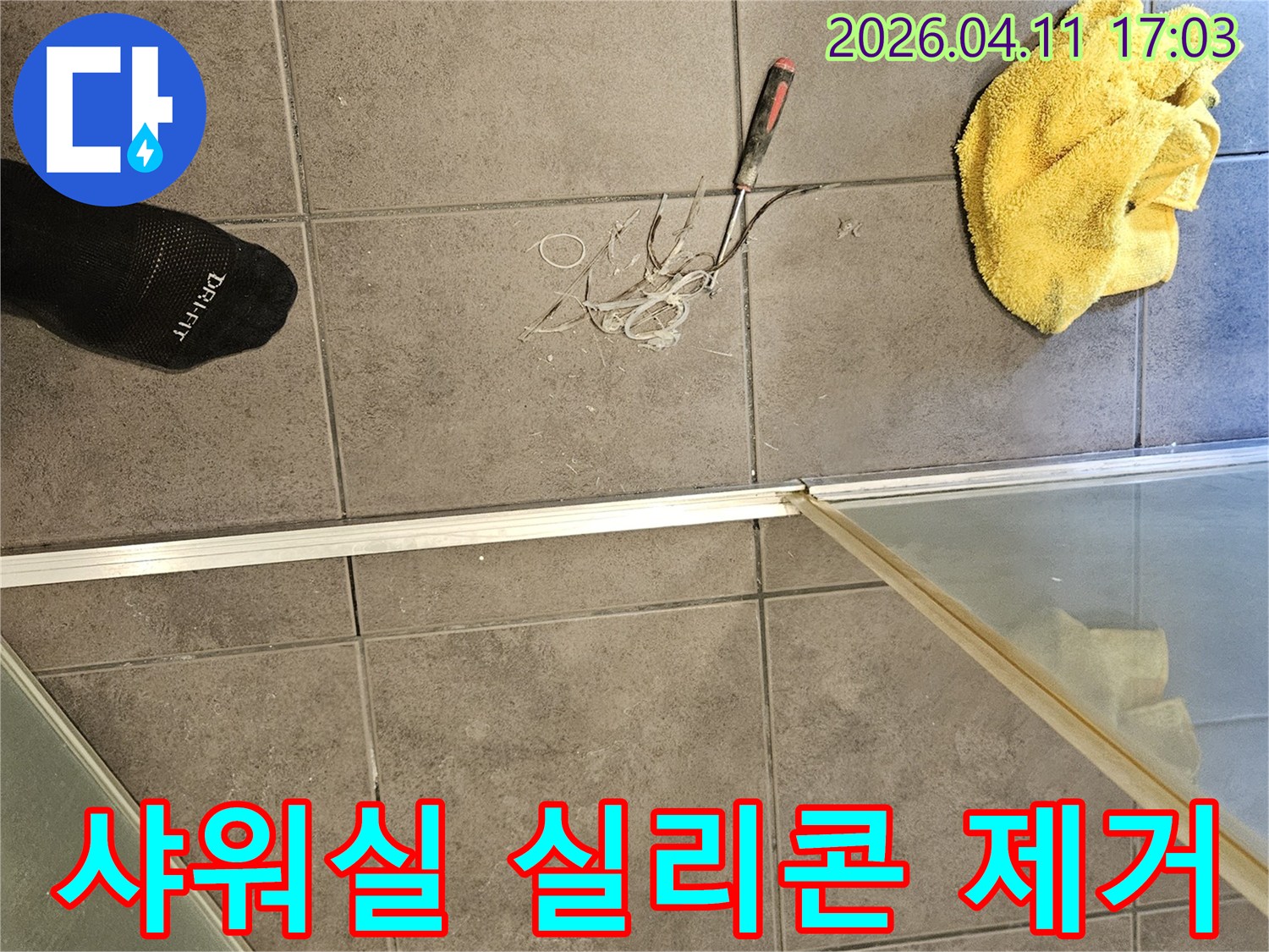 욕실 바닥 타일 위-노란 수건과 공구-그리고 샤워실 경계면의 낡은 실리콘을 제거하는 모습