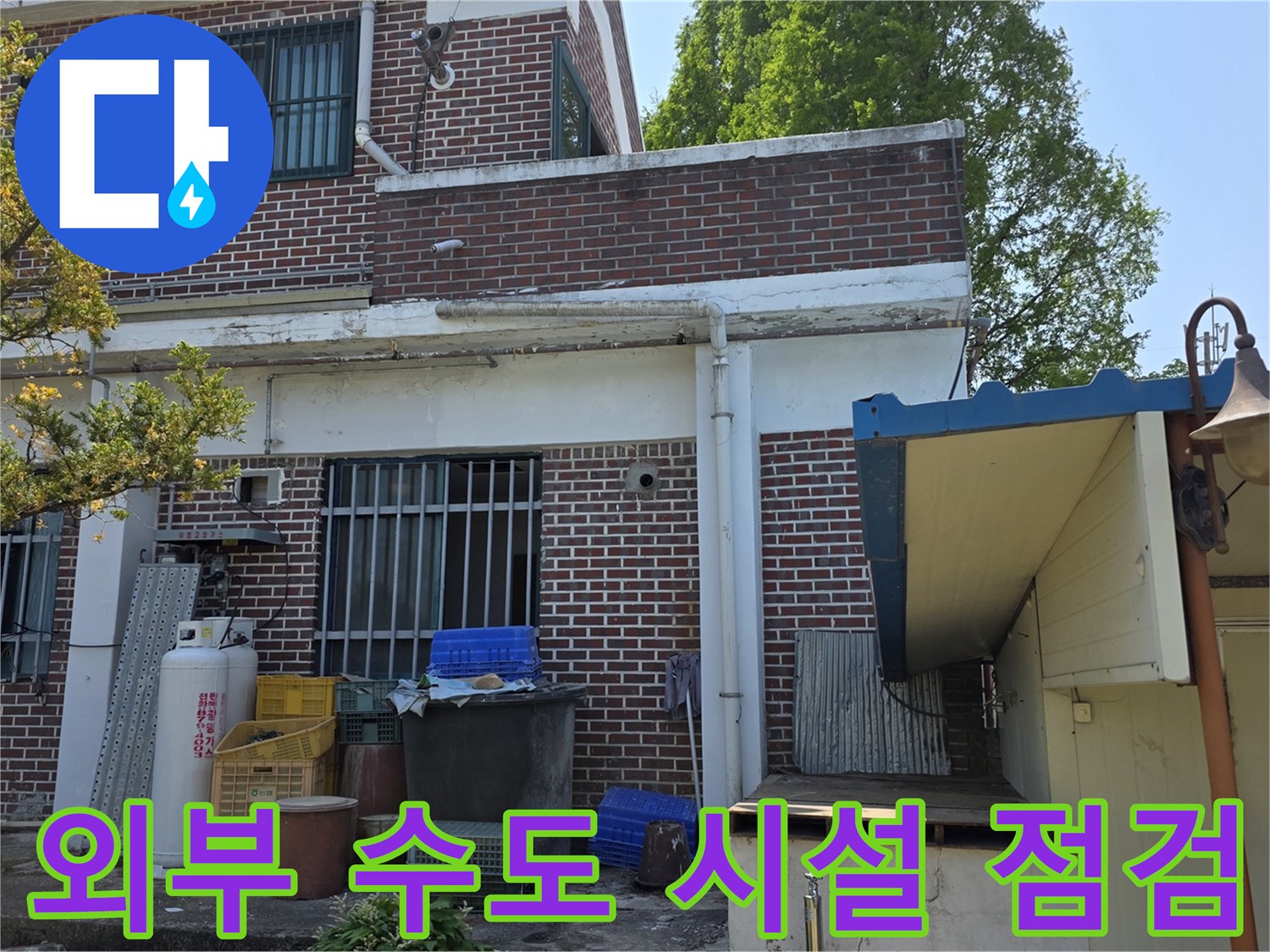 건물 외벽 하단의 외부 수도꼭지와 배관 연결 부위를 촬영한 이미지입니다.