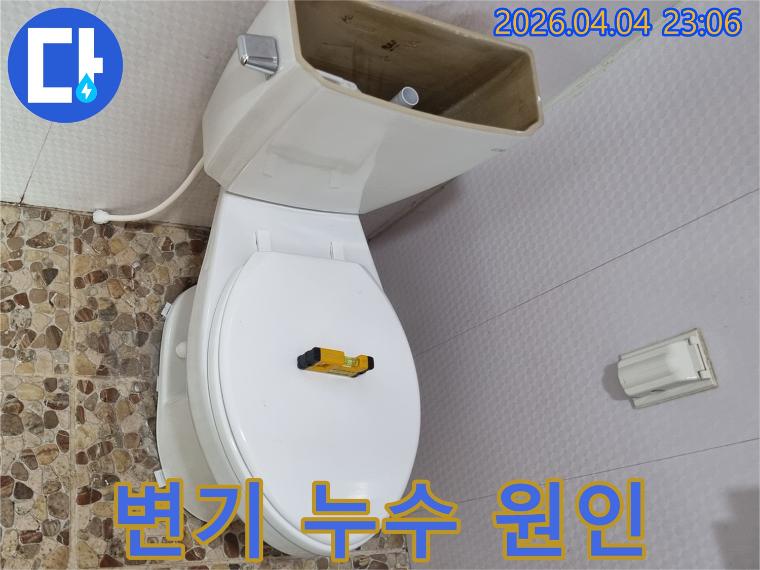 변기 물탱크 덮개가 제거된 상태로-내부 부품이 노출되어 있으며-수평계가 변기 시트 위에 놓여 있습니다