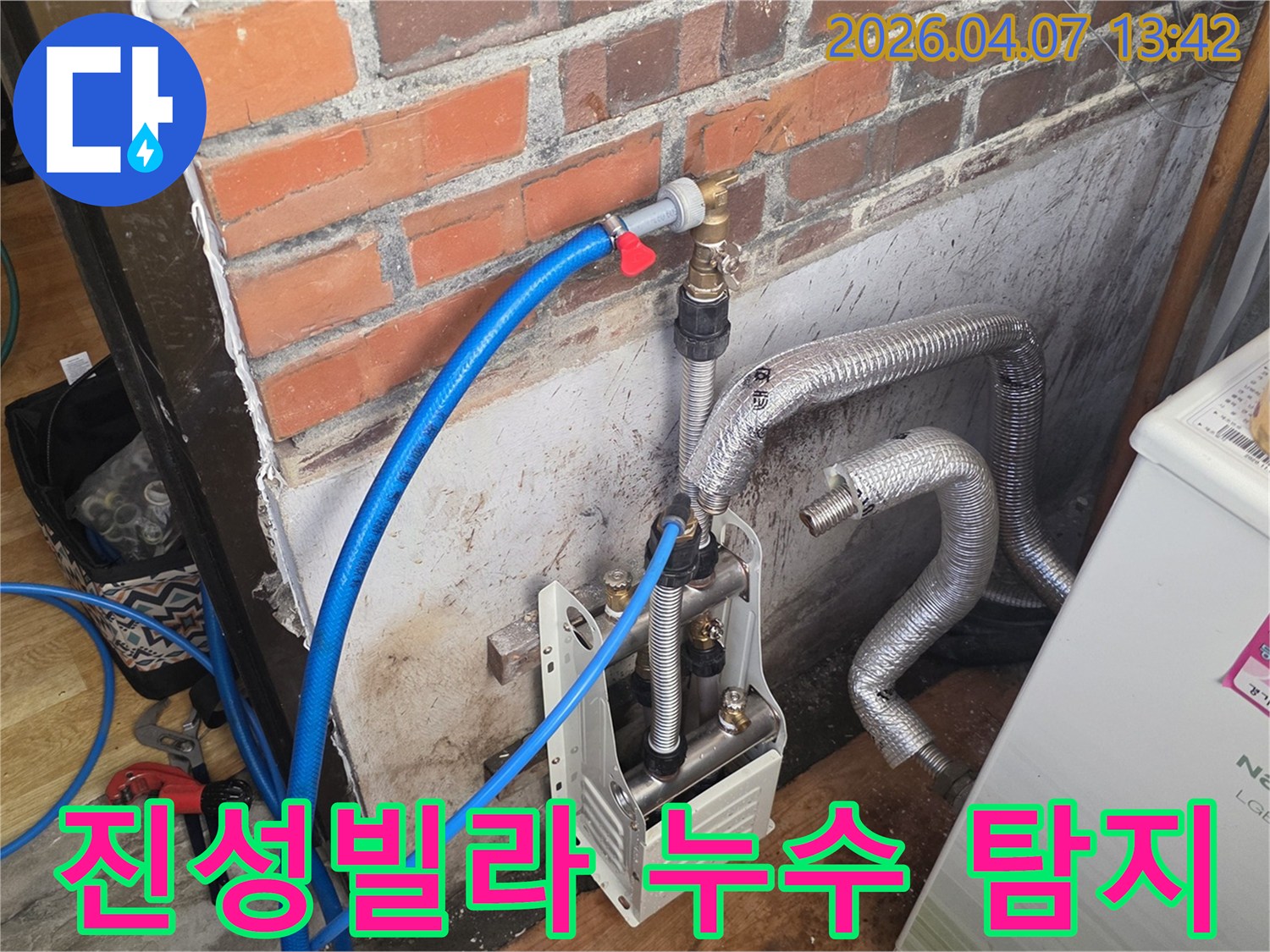 포천 일동면 진성빌라의-벽돌 벽 옆에-누수 탐지 장비와-배관들이 설치되어 있으며-정밀한 누수 진단이-진행되고 있는 모습입니다.