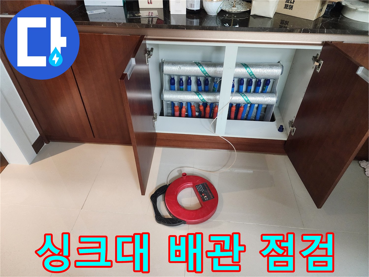 싱크대 하부장 내부의 보온재로 감싸진 배관들과 거리 측정용 트레이스 휠