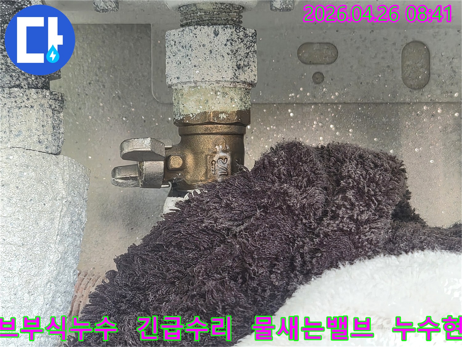 오래된 수도 밸브에서 부식과 함께 물이 새는 모습이 선명하게 보이는 사진-수건으로 물기를 흡수하고 있는 현장-누수 문제의 심각성을 보여줍니다