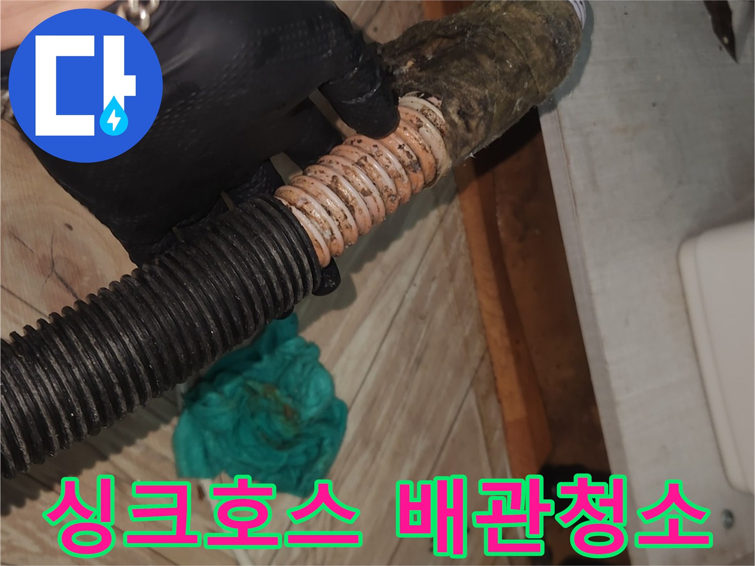 검은 장갑을 낀 손이-오랜 사용으로 오염된 싱크대 배수 호스를-들어 올린 채-석션 클리닝을 시작하려는 장면