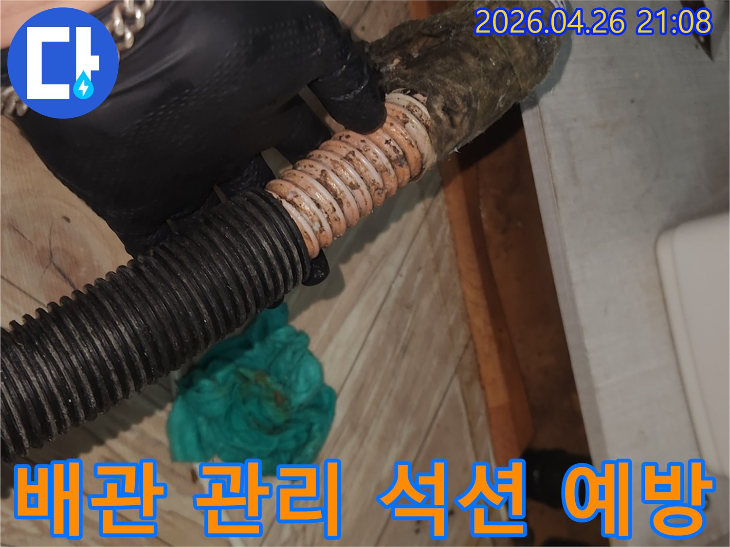검은 장갑을 착용한 기술자가-오염된 싱크대 배수 호스를-석션 장비로 깨끗하게 청소하여-누수를 사전에 예방하고 관리하는 모습