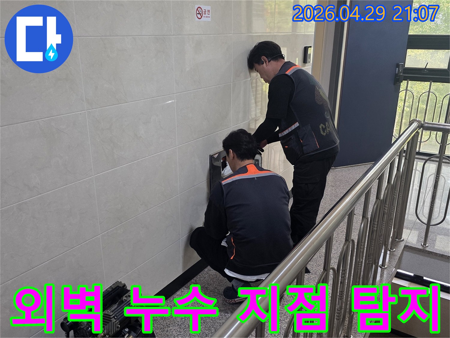 두 명의 전문 기술자가 건물 벽면의 외벽 누수 의심 지점을 정밀하게 탐지하고 있습니다-건물 안전과 내구성을 위한 정확한 원인 파악 작업입니다.