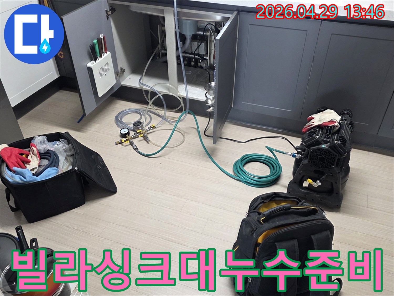 동안구 빌라의 주방 싱크대 하부에서-누수 탐지를 위한-압력 게이지와 호스-그리고 공기 압축 장비를-설치하는 작업이 진행 중입니다
