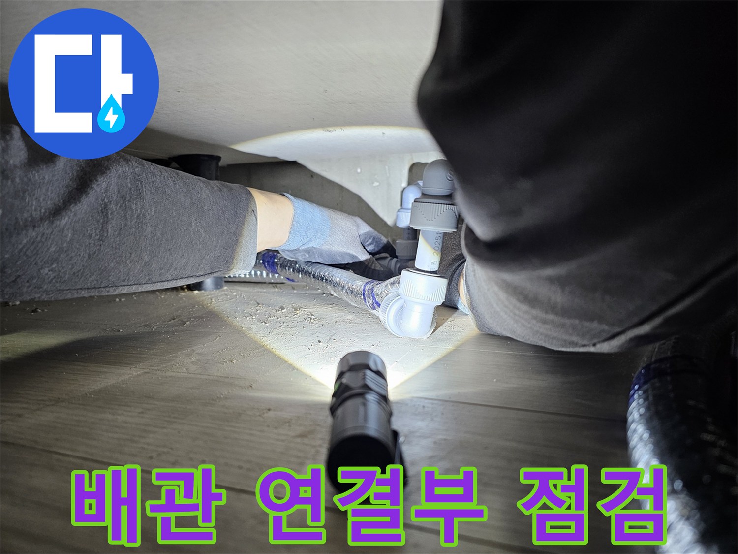 누수-탐지-전문가가-손전등을-사용하여-어두운-배관-아래를-정밀하게-살피는-장면