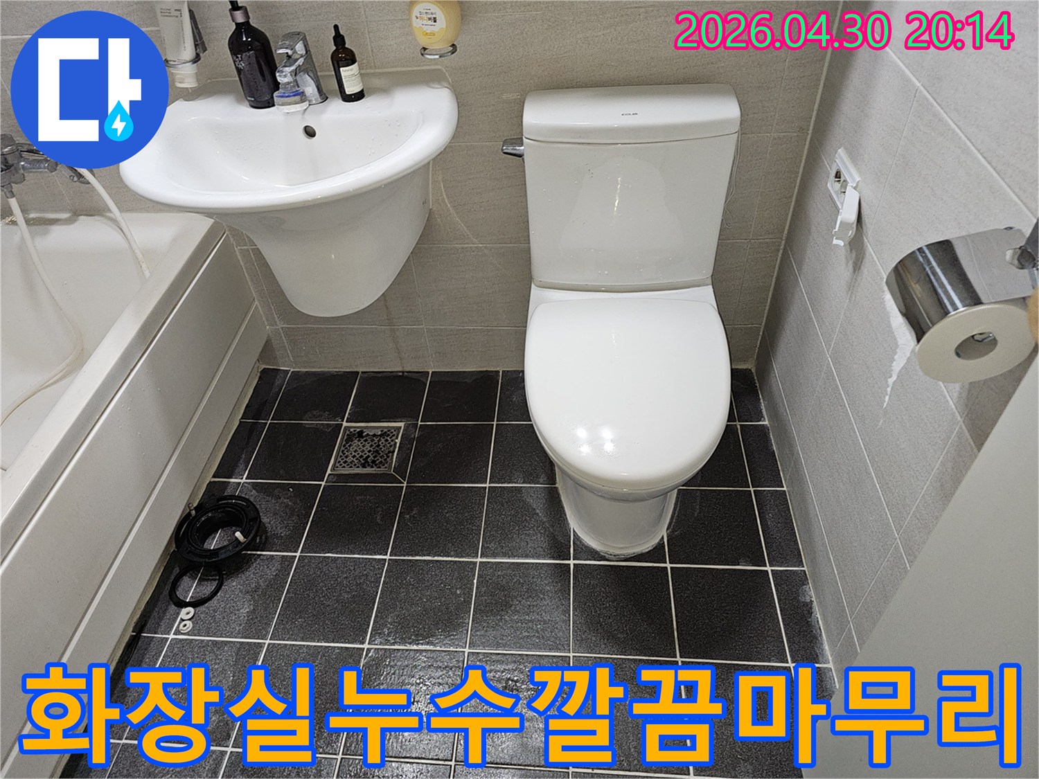 누수 수리 후 말끔하게 정돈된 아파트 화장실의 전경을 보여주는 사진입니다-새로운 변기와 세면대가 설치되어 있으며-어두운 색상의 바닥 타일이 깨끗하게 마감되었습니다