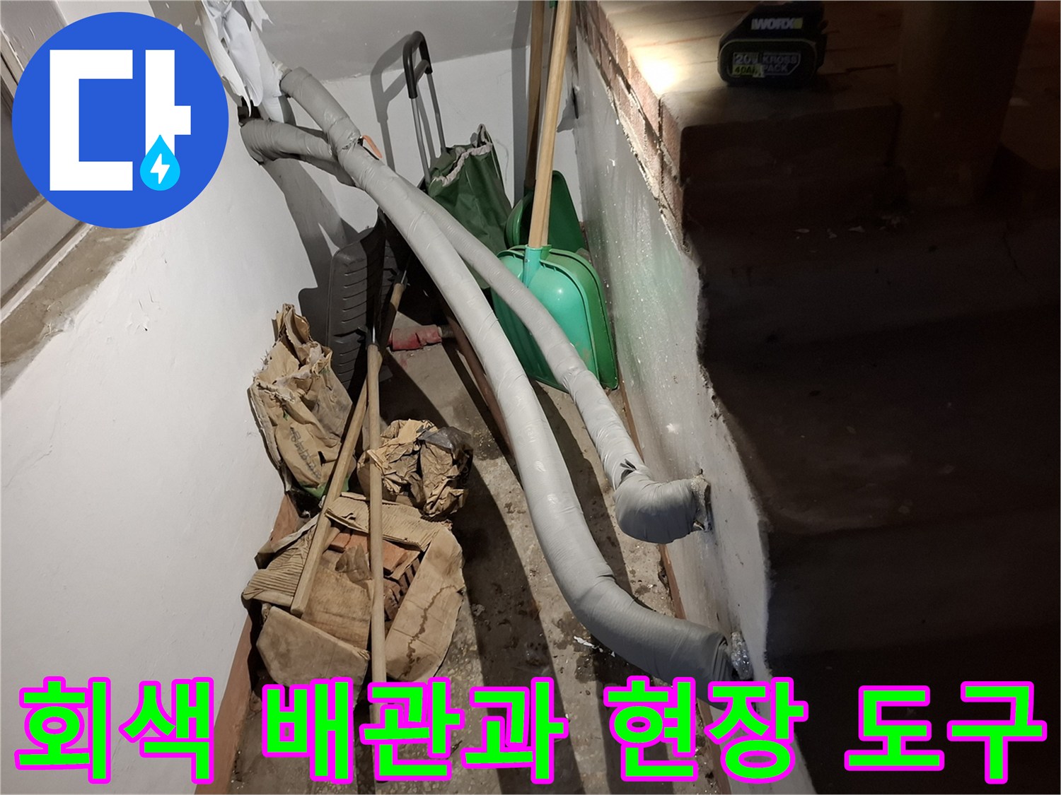 벽면에 고정된 회색 배관과 바닥의 작업용 자재들