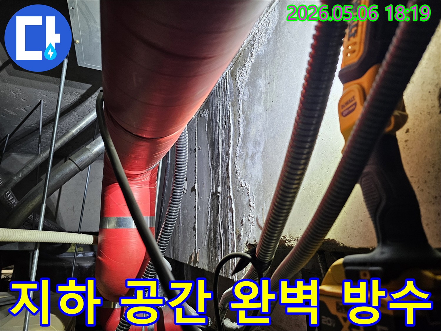 어두운 지하 공간에서-빨간색 배관과-습기로-얼룩진-벽면을-촬영한-사진으로-누수 해결을-위한-방수 공사-전-상태를-보여줍니다