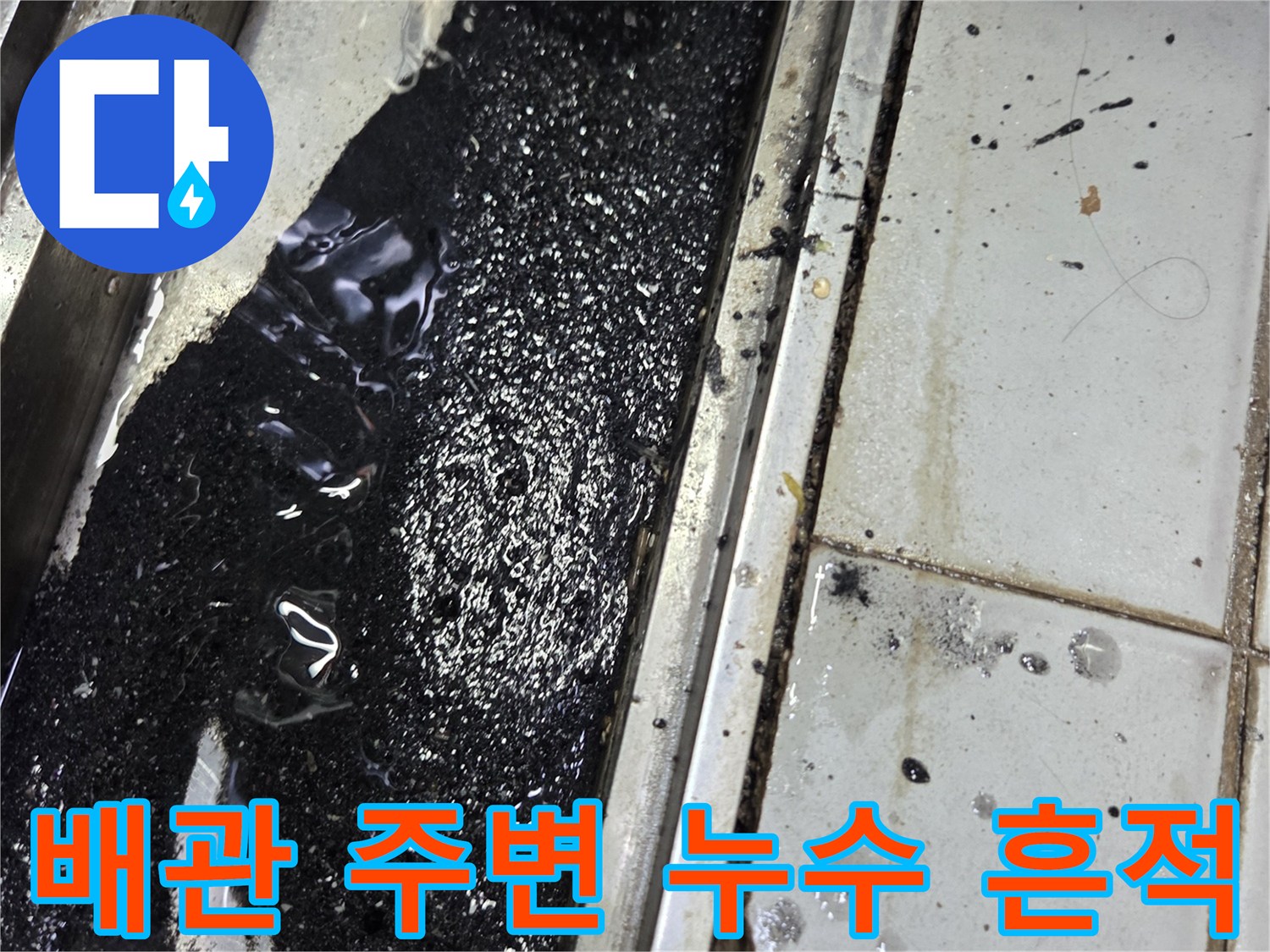 타일 틈새로 스며 나온 검은색 액체와 노출된 배관 연결부