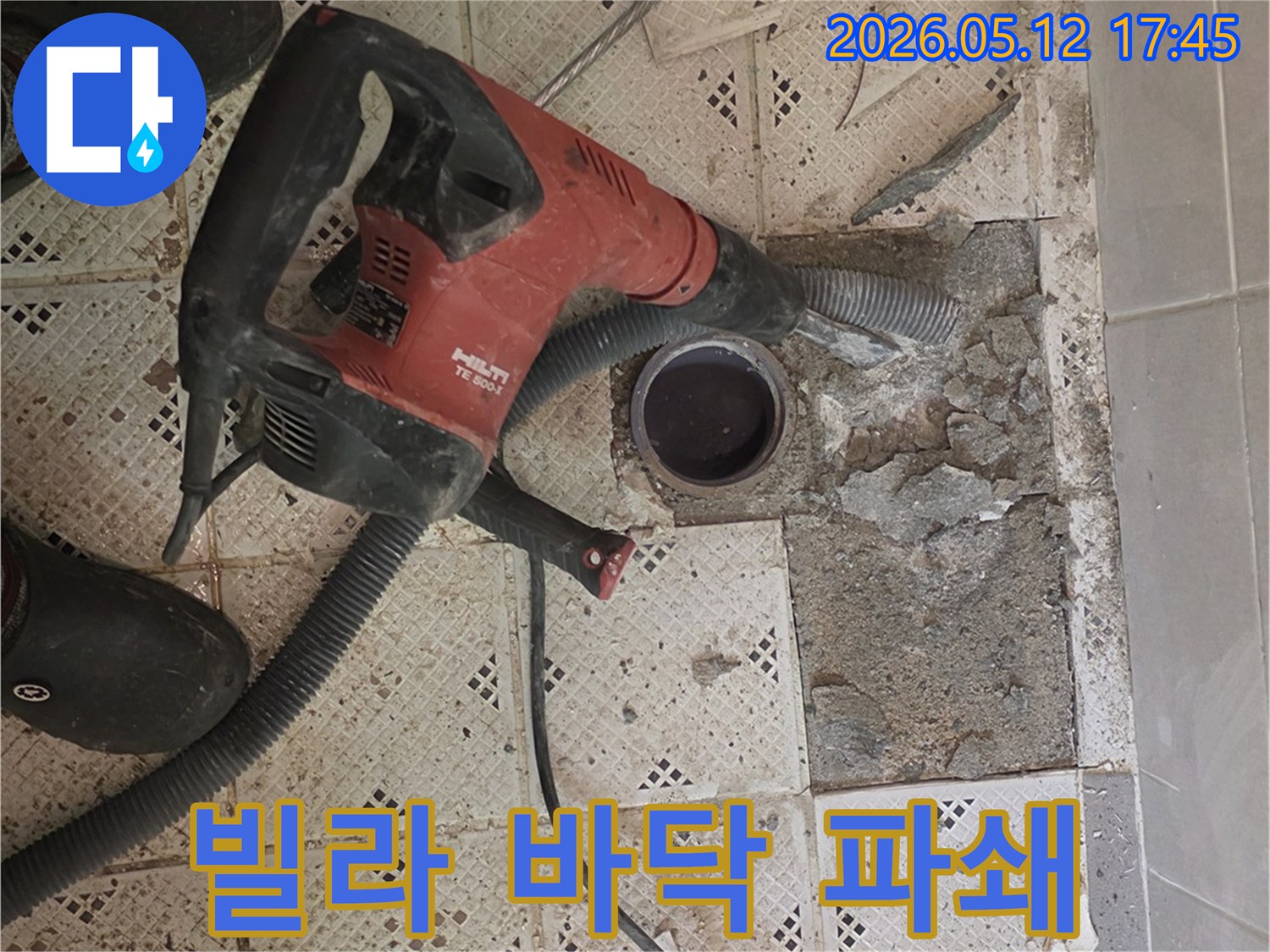 빌라 누수 탐지를 위해-바닥 타일을 깨고 있는-강력한 파쇄 장비와-작업자의 발이 찍힌-현장 사진입니다.
