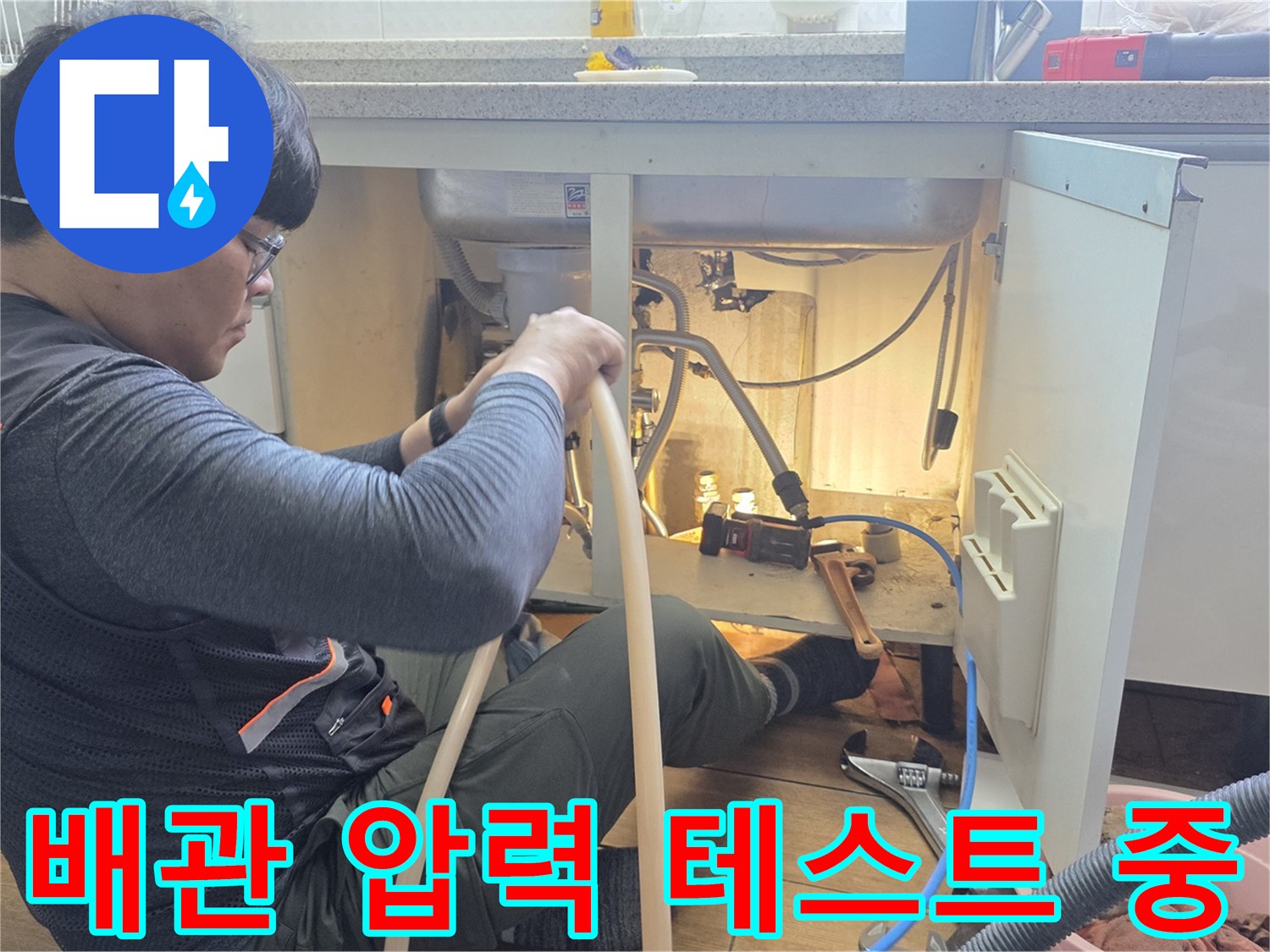 싱크대 하부 공간에서 분배기 배관에 공압 호스를 연결하여 점검하는 모습