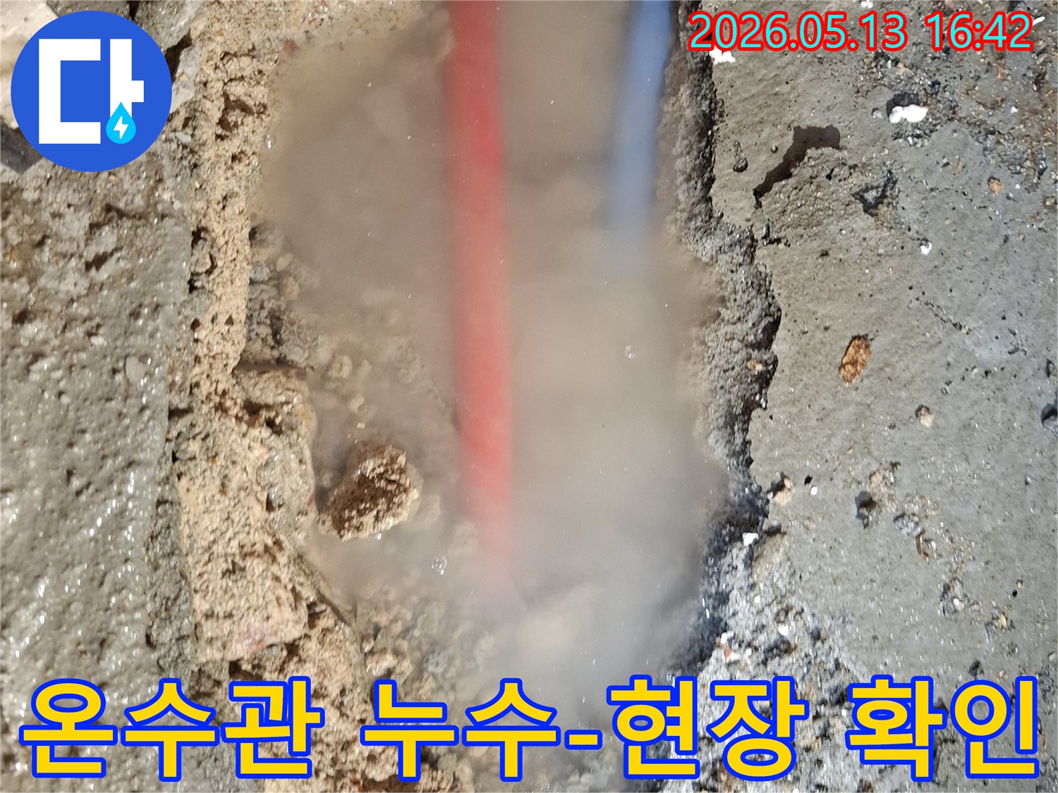흙탕물 속에서-붉은색과 푸른색 배관이-보이는 누수 현장으로-수증기가 활발하게 뿜어져 나오는-긴급한 상황을 보여줍니다