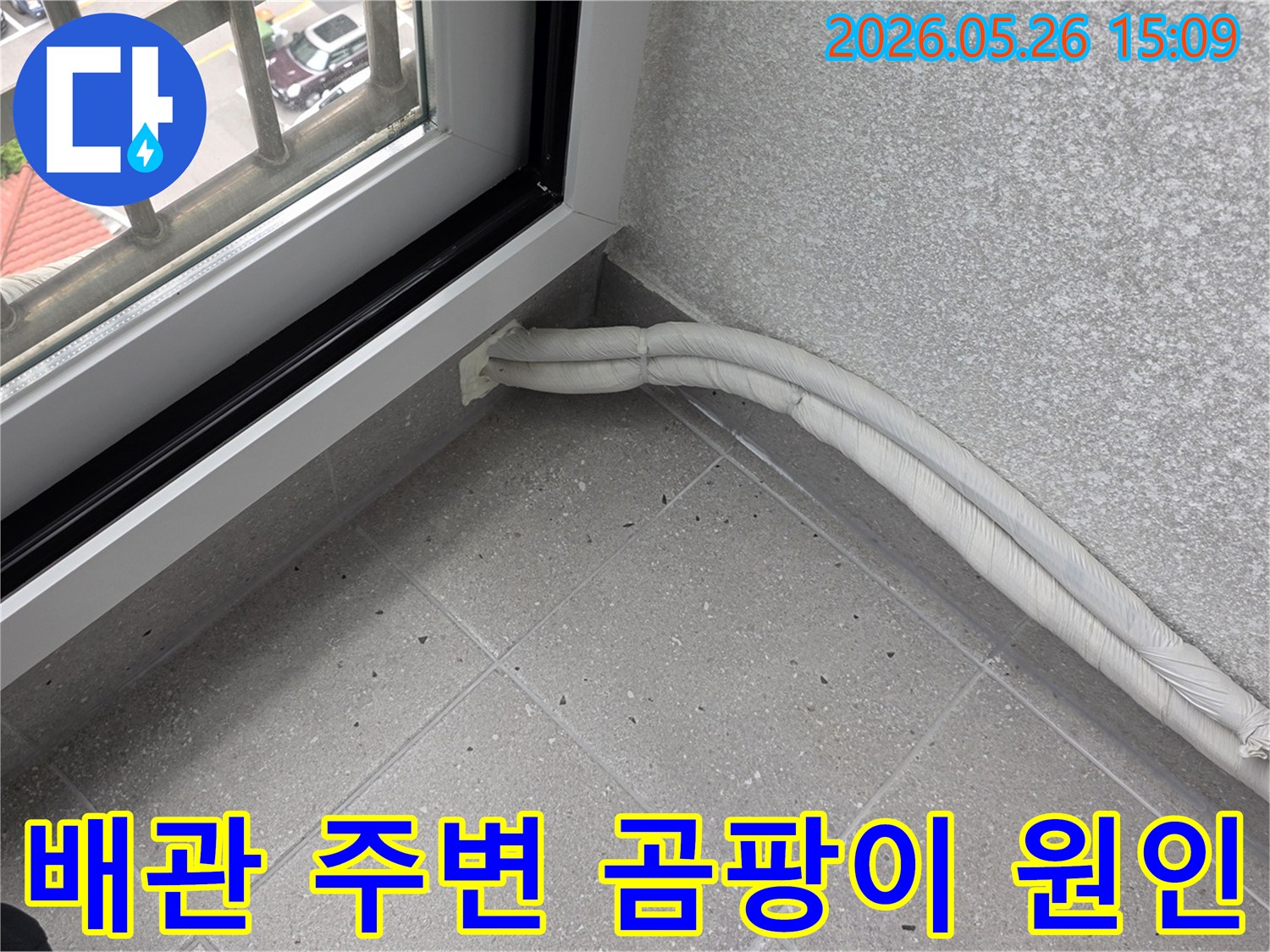 창문 옆 바닥에-보온재로 감싸진-두 개의 배관이-설치된 모습으로-배관 주변의-습기와 곰팡이-발생 가능성을-확인합니다.