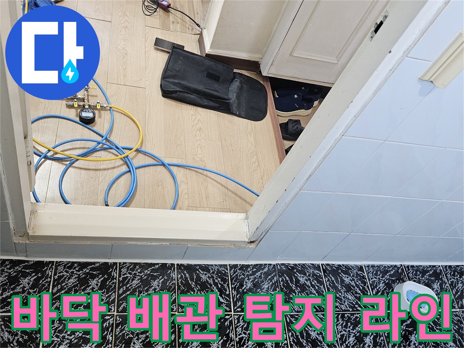 현관 바닥 타일 위에 펼쳐진 파란색과 노측 색상의 배관 점검용 호스