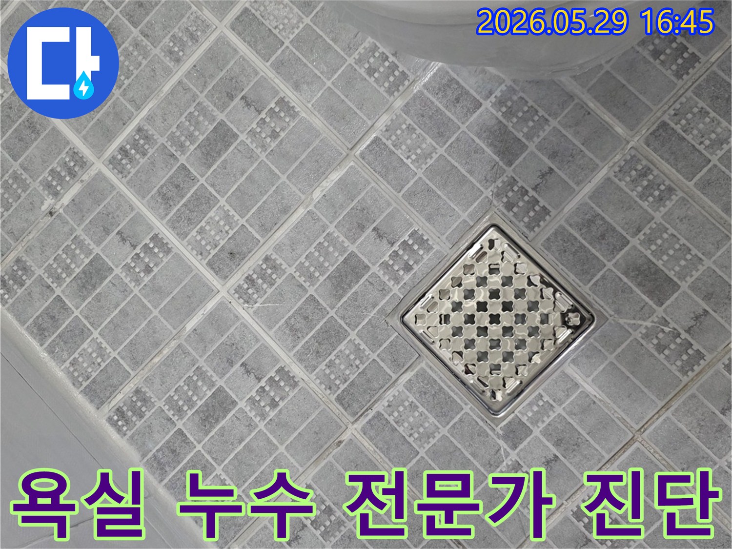 회색 패턴 타일로 덮인 욕실 바닥과-중앙의 스테인리스 배수구-그리고 변기 하단부가 보이는-전문가 누수 진단 현장