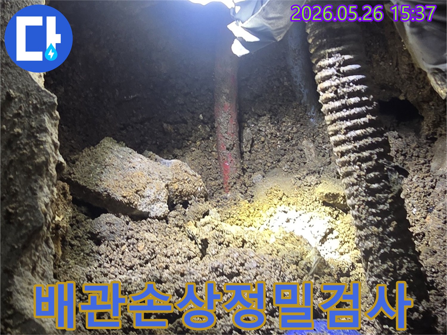 누수-전문가가-어두운-굴착-현장에서-손전등으로-배관의-손상-부위를-정밀하게-검사하는-과정