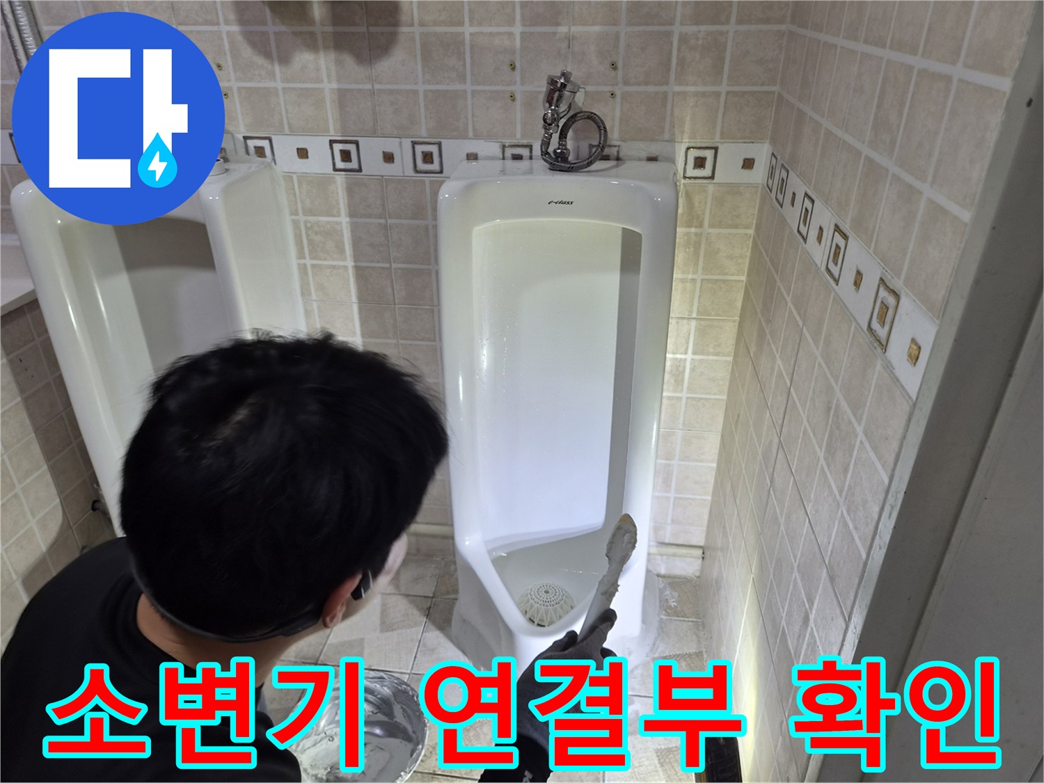소변기 아래쪽 배관과 타일 경계 부위를 자세히 살펴보는 모습입니다.