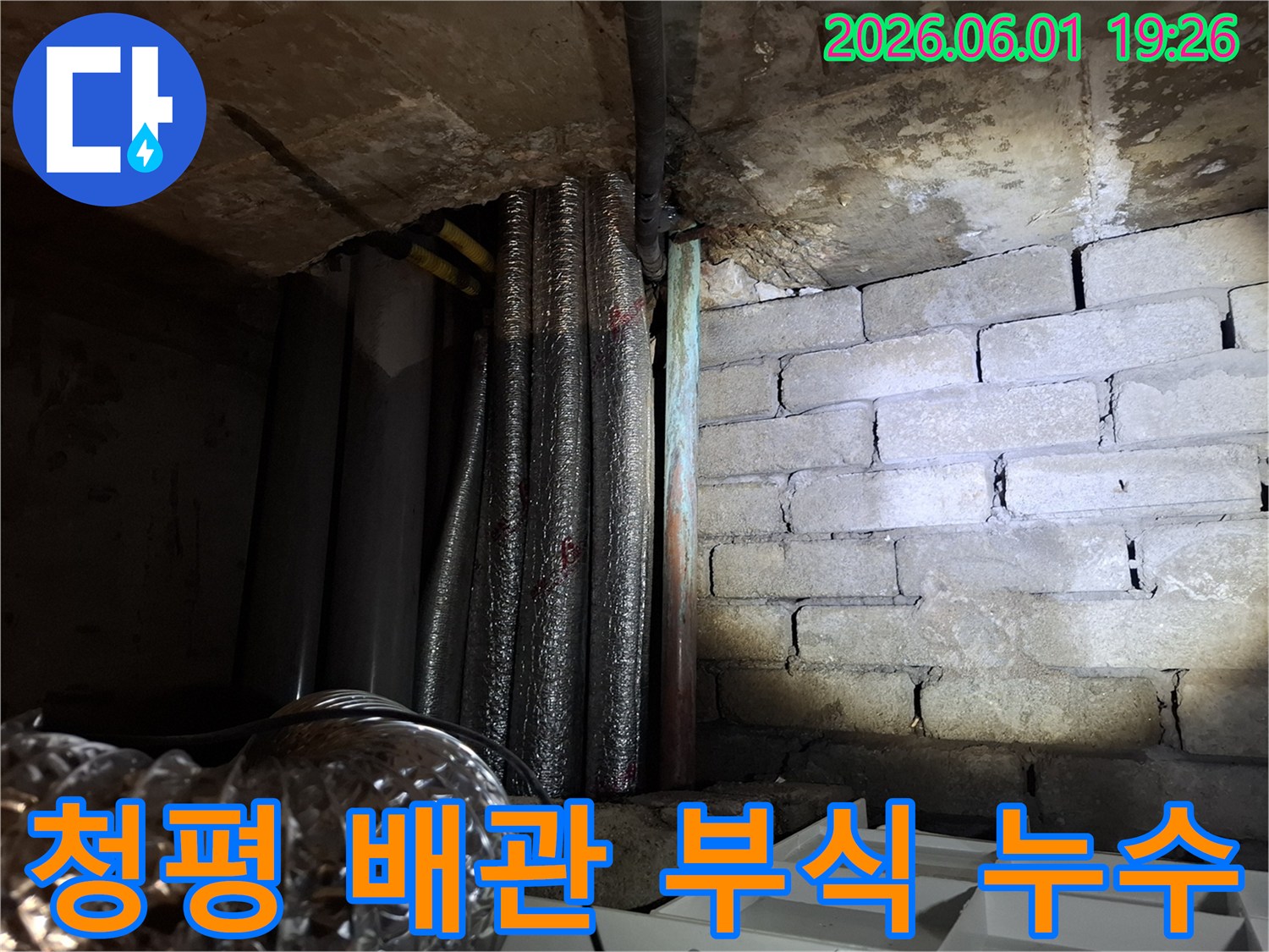 어두운 지하 공간에서-부식된 배관과-물에 젖은 벽돌 벽면이-보이는 누수 현장입니다