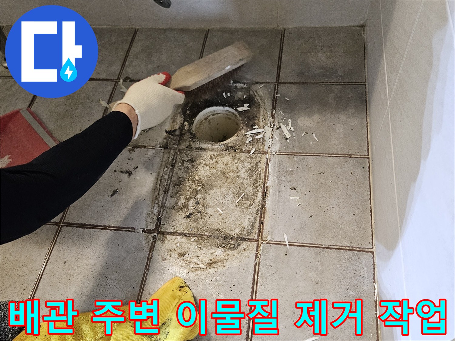 작업자가 도구를 사용하여 변기 배관 주변의 낡은 마감재를 정리하고 있습니다.