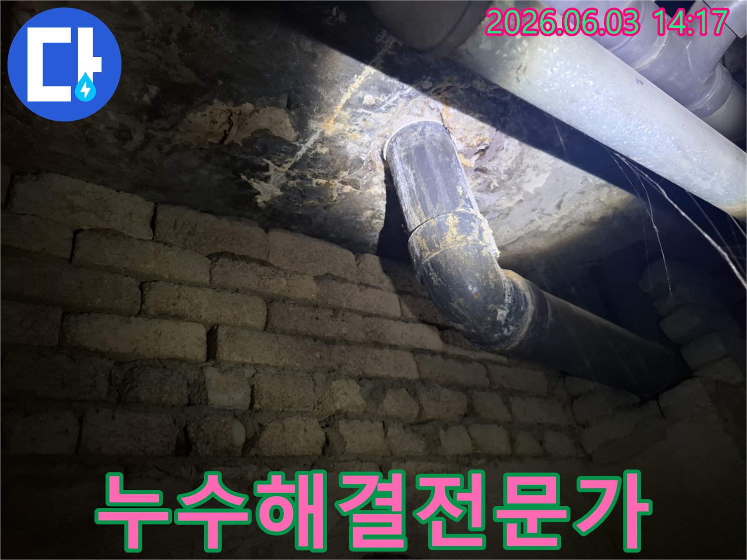 어두운 지하 공간의-낡은 벽돌 벽과-오래된 배관 주변에서-발견된 누수 흔적을-조명으로 비추어-정밀하게 진단하는 모습