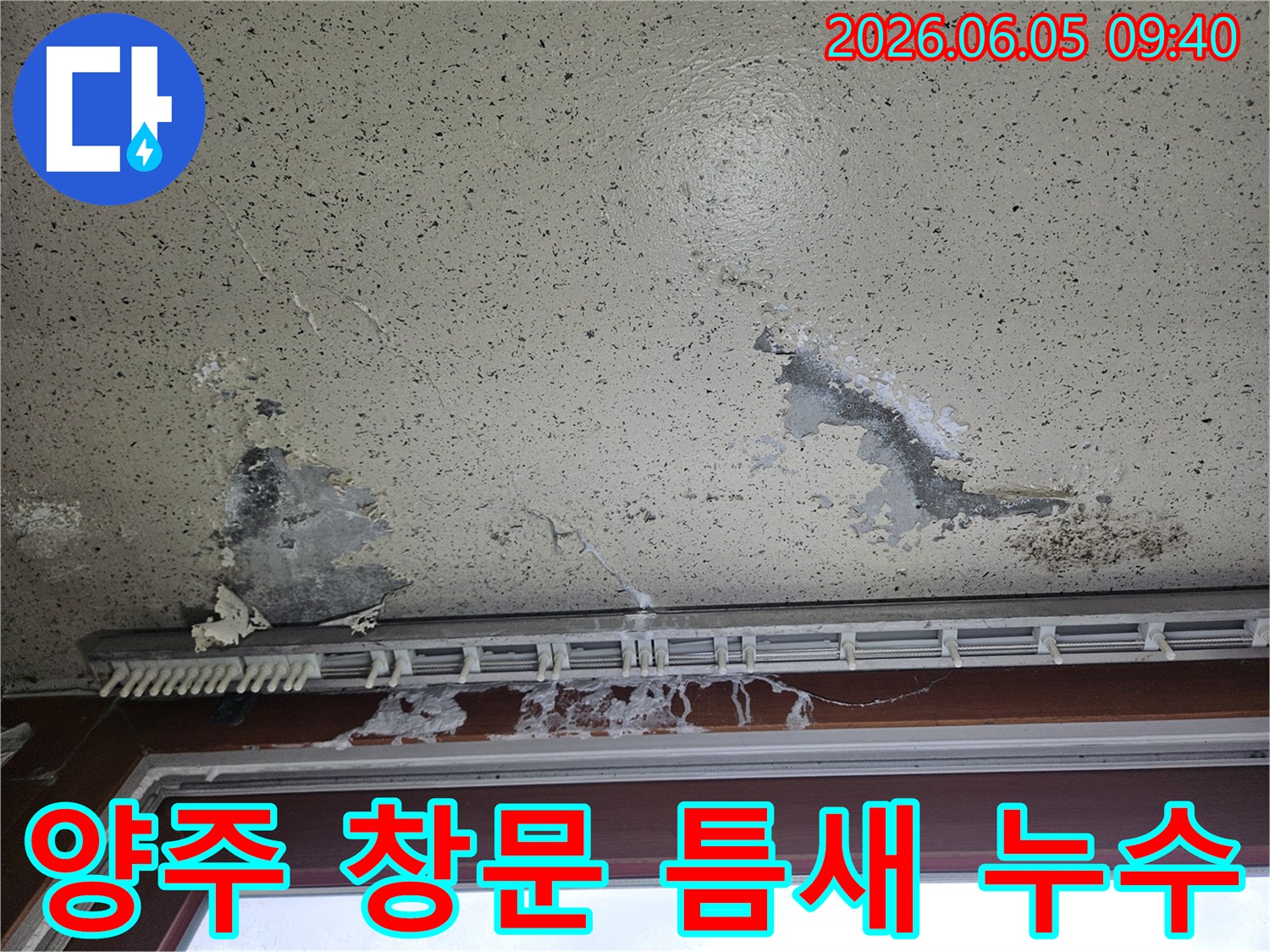 아파트 창문 틈새 주변 벽지가 물에 젖어 변색되고-얼룩이 진 모습으로-창문 틈새로 유입된 빗물 누수 피해를 보여줍니다.