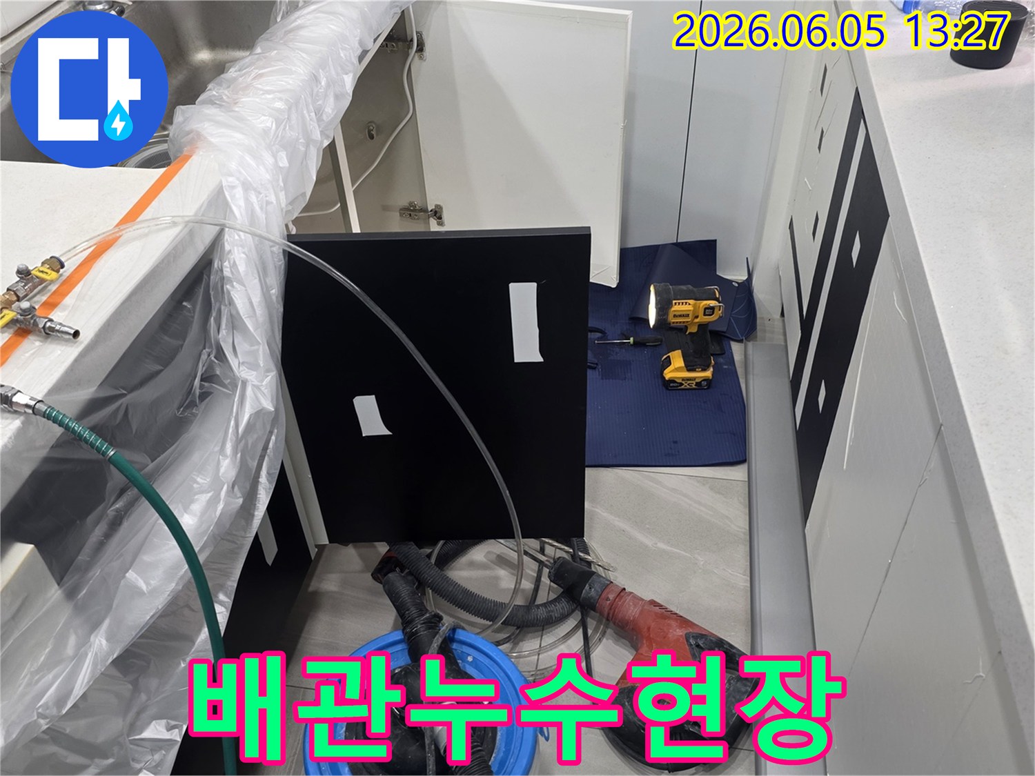 주방 싱크대 아래에서 누수 작업을 진행하며-주변을 보호하고 있는 현장 사진입니다.