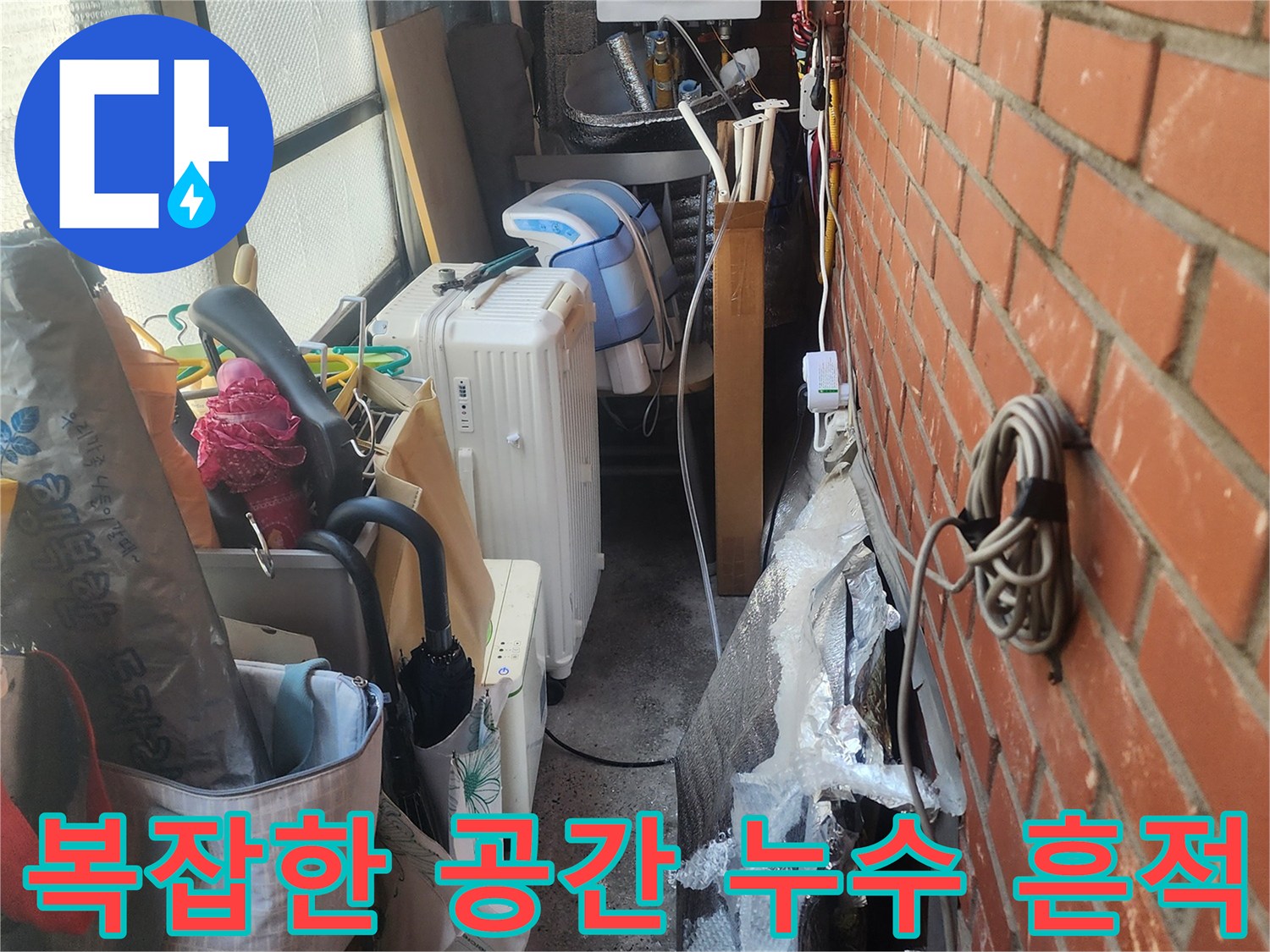 벽돌-벽-아래-복잡하게-얽힌-배관과-생활-용품들-사이에서-발견된-누수-흔적을-보여주는-사진