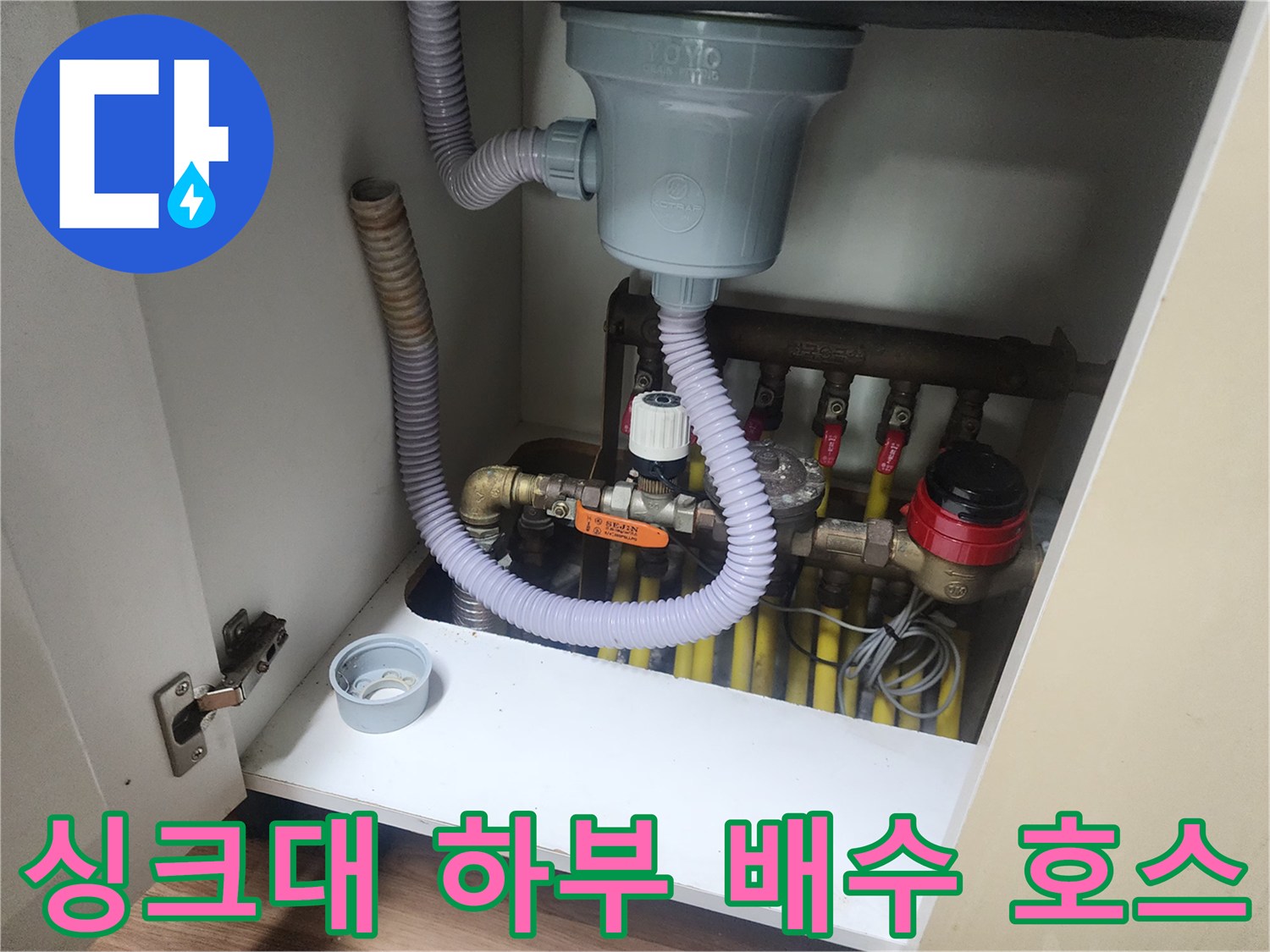 회색 주름관과 노란색 배관들이 연결된 싱크대 아래쪽 모습